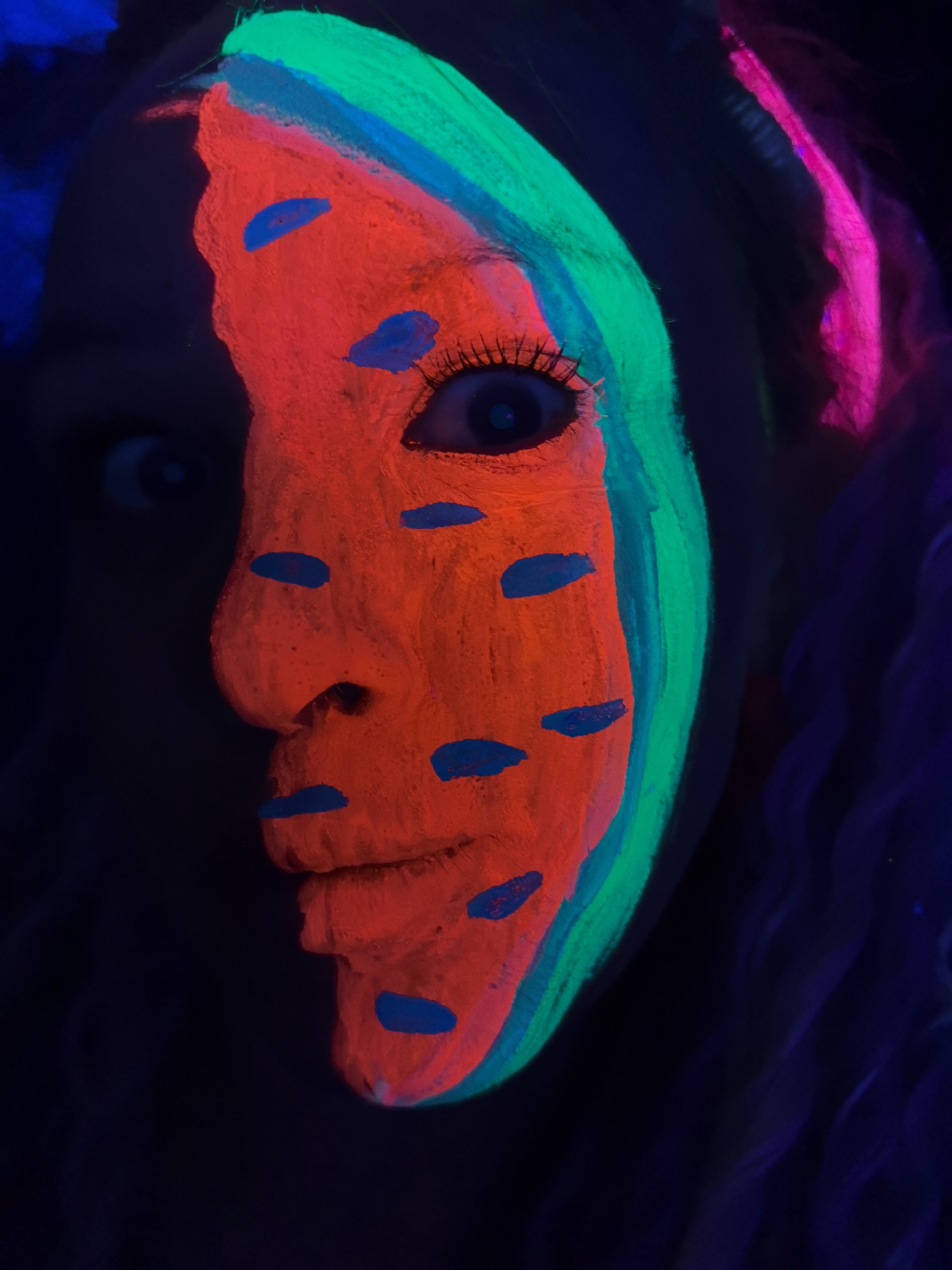 UV-lit watermelon face paint art captured in Noviy, Russia