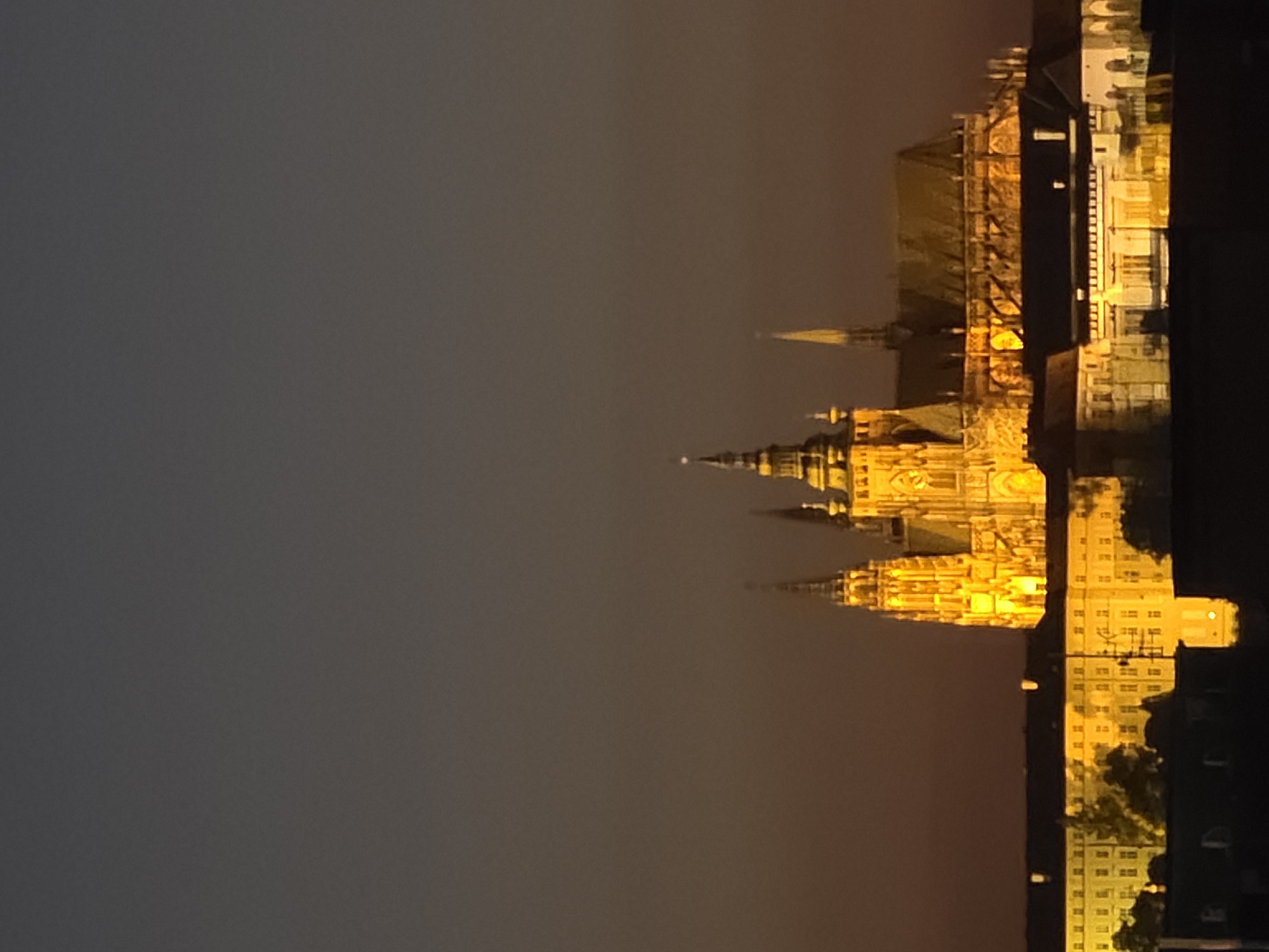 Nighttime cityscape observed with illuminated cathedral, tram, pedestrians