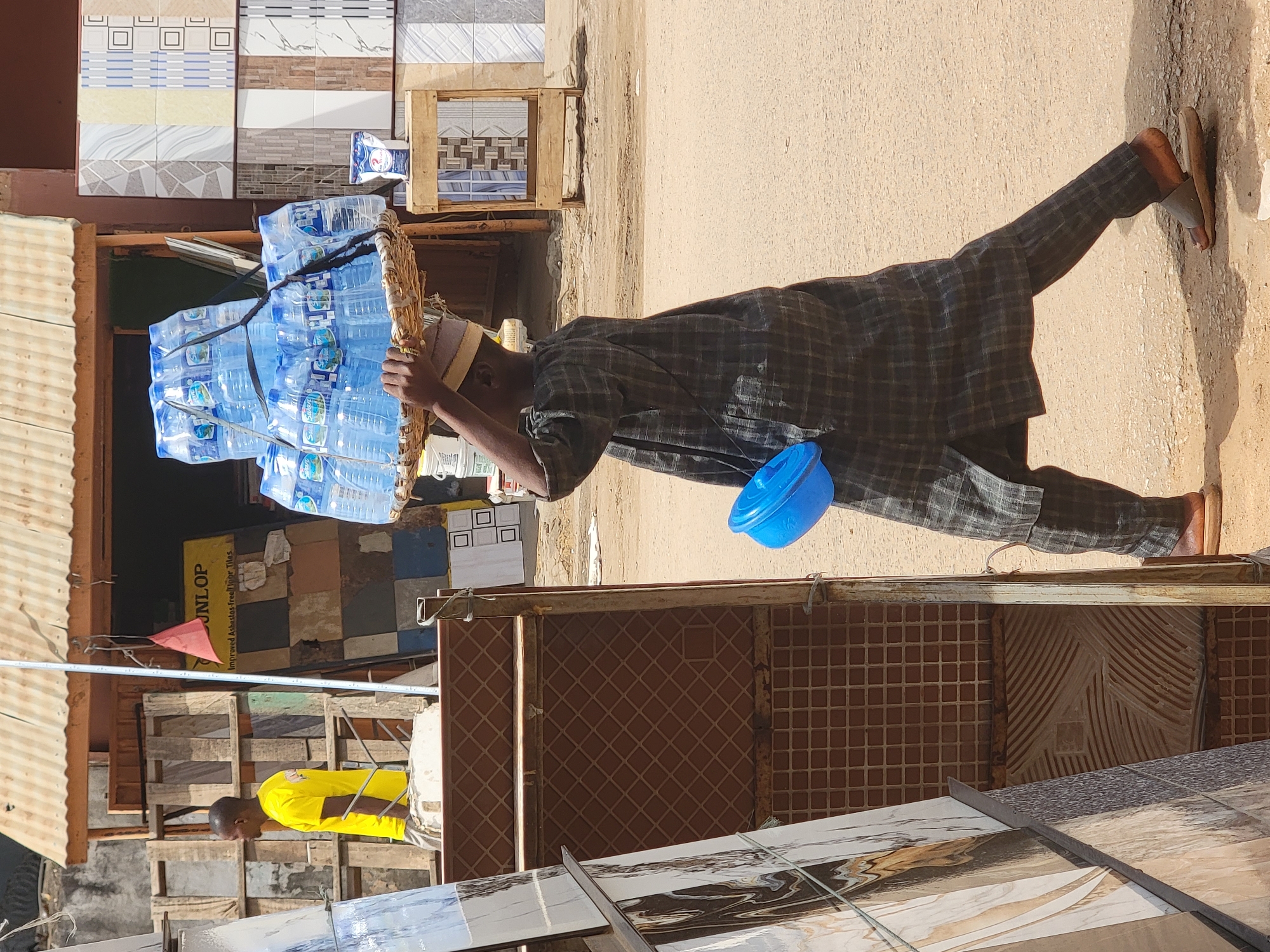 Men carry water bottles and clothing goods in Maiburiji