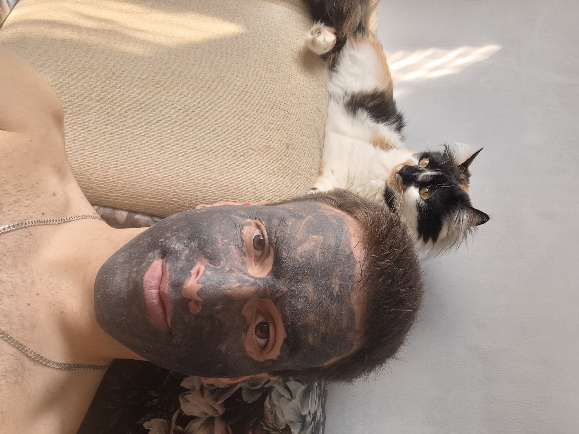 Man in face mask rests with calico cat indoors