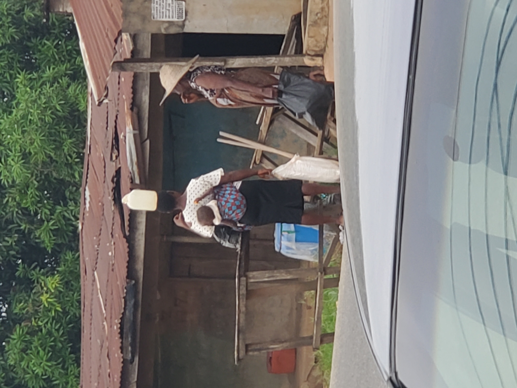 Person carries baby, balances container; white rooster found resting