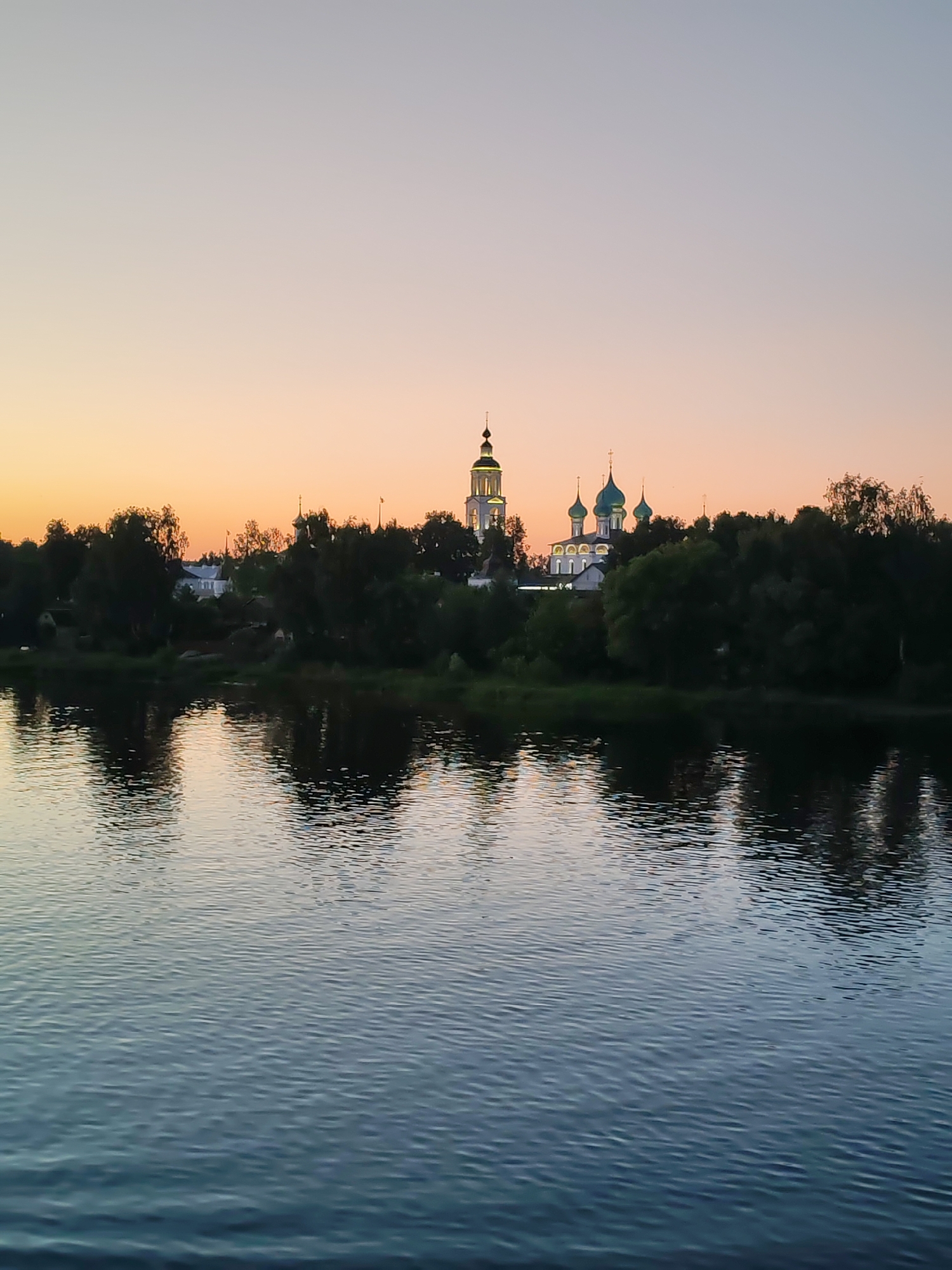 Dusk settles over a river with a church on the far bank.