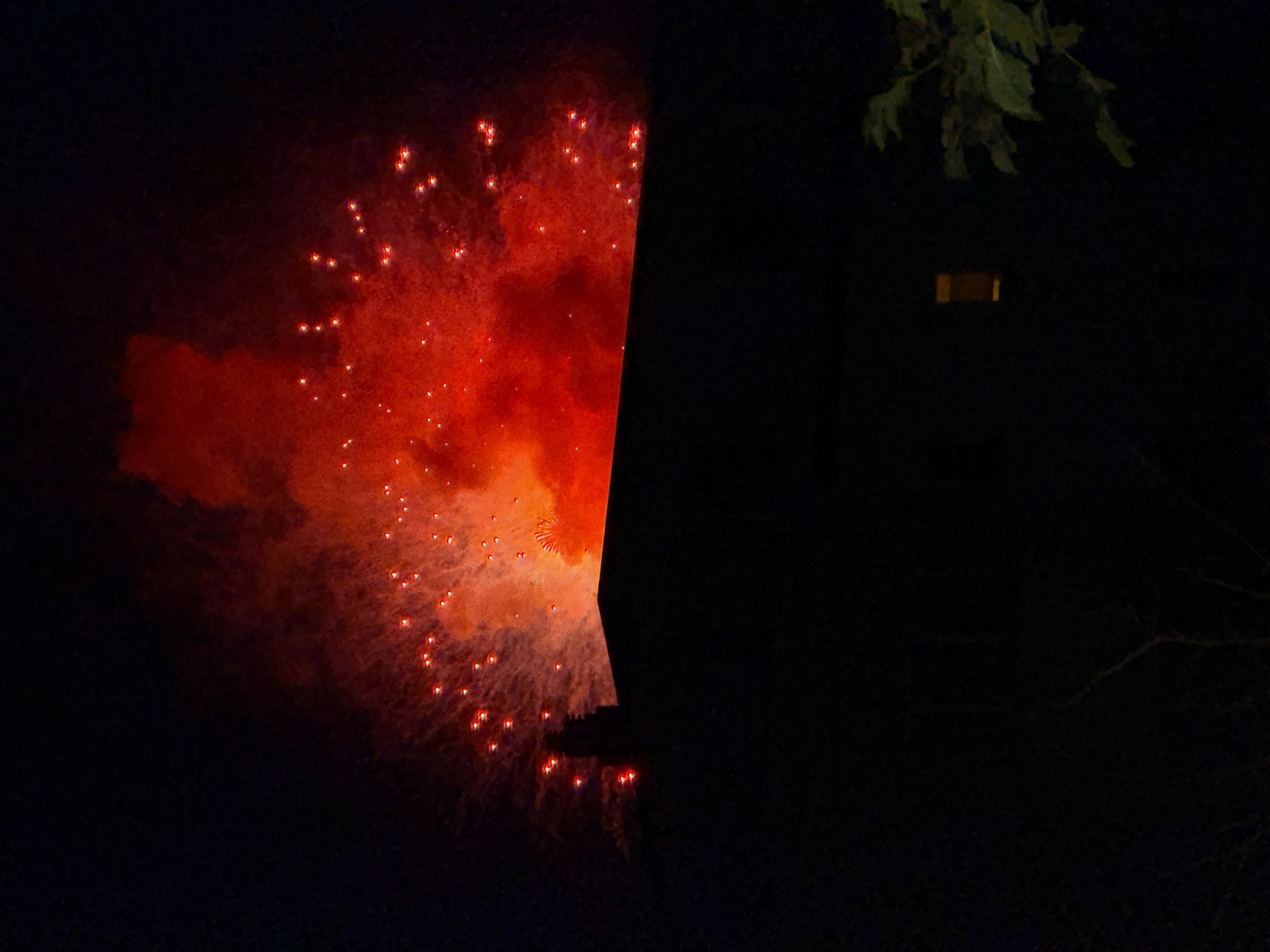 Nighttime fireworks burst over a residential building in colorful display