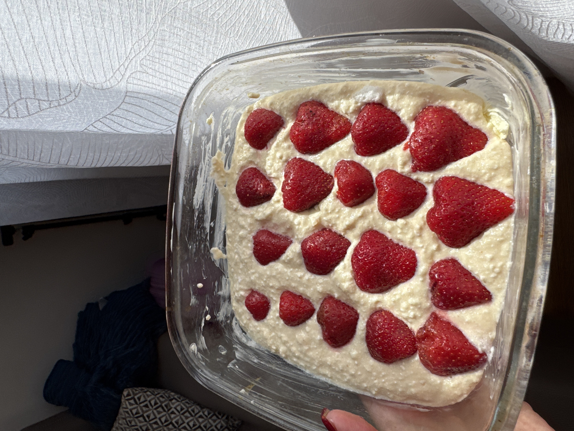 Person prepares strawberry dessert in glass baking dish