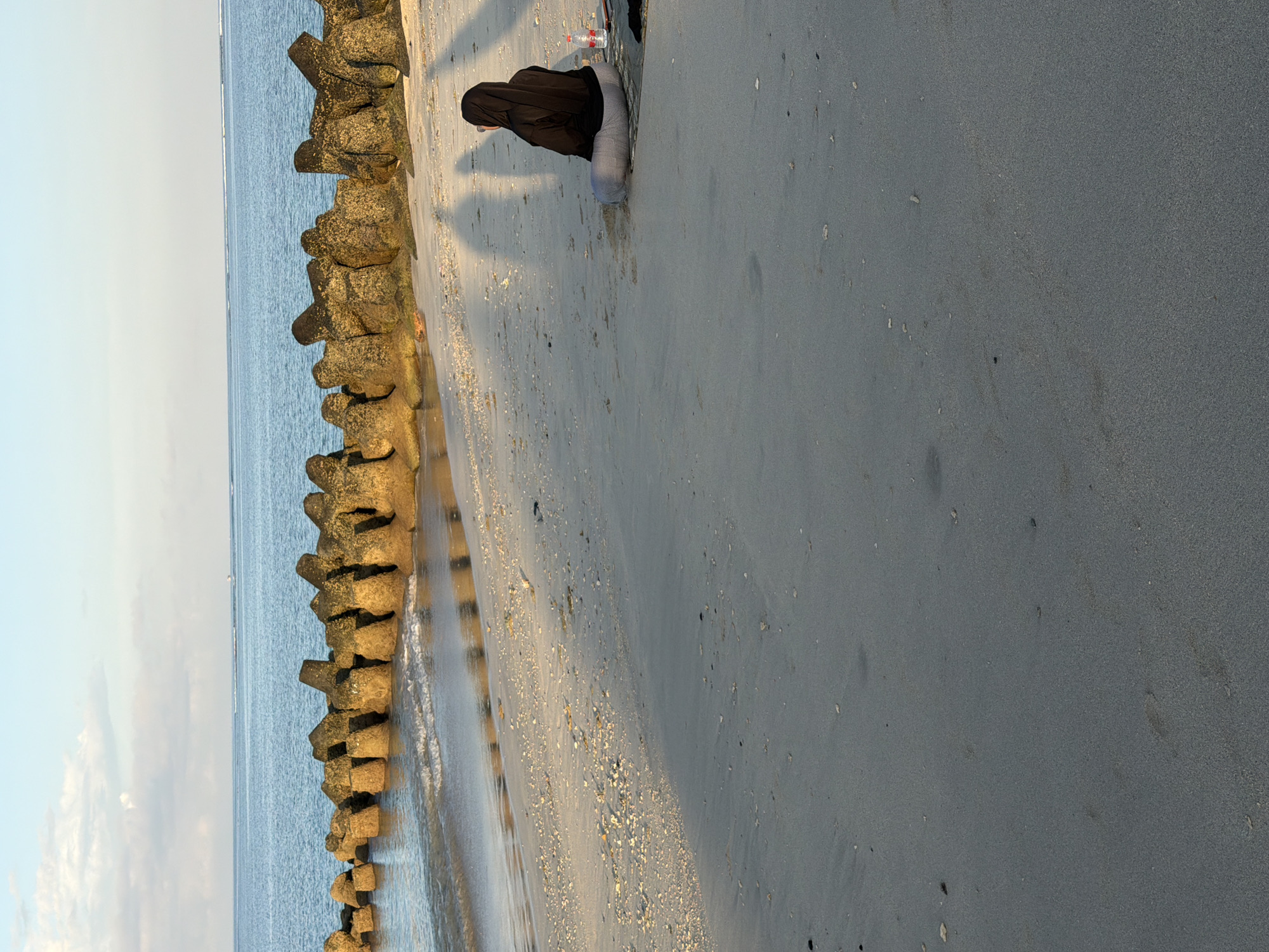 Woman in hijab sits by breakwater at Kuta Beach