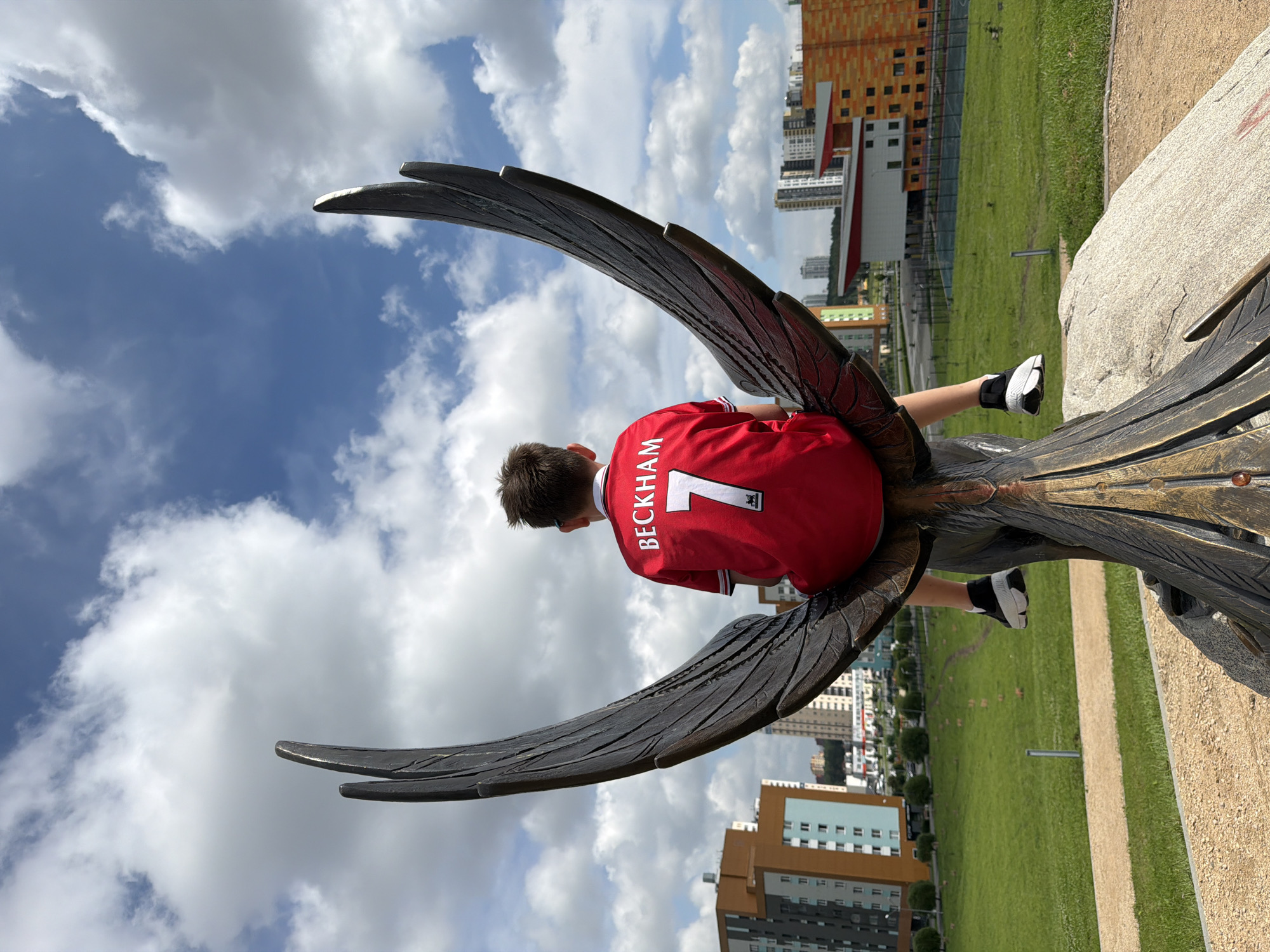 Climbing a bronze phoenix sculpture in Yekaterinburg, Beckham jersey on