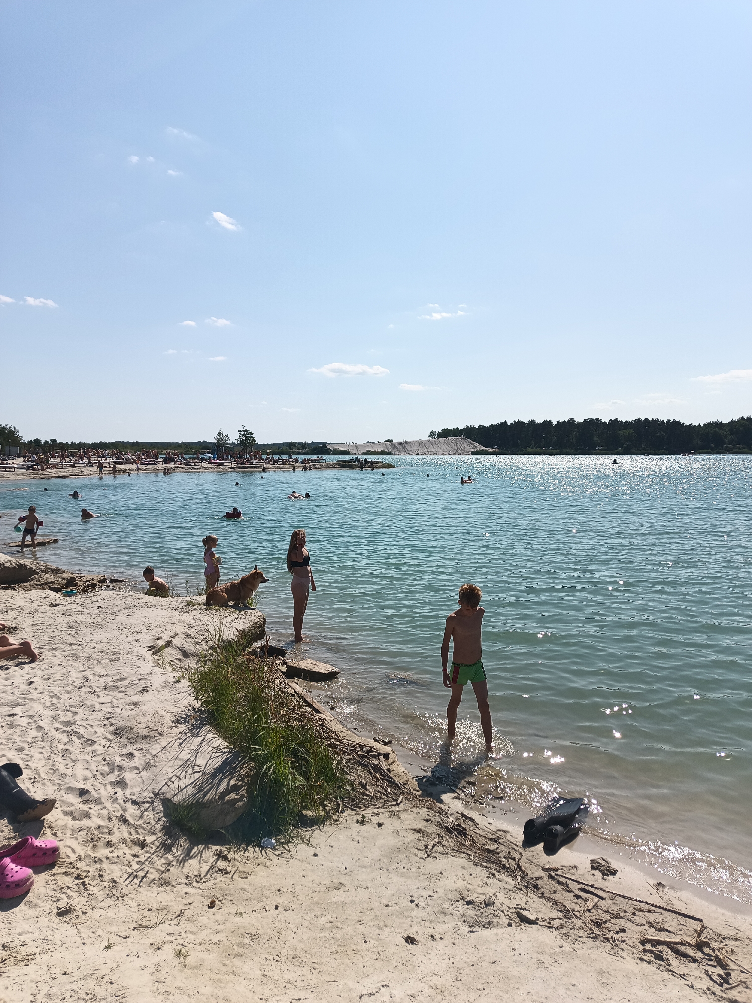 Sunny day at a turquoise quarry lake with swimmers and ATVs