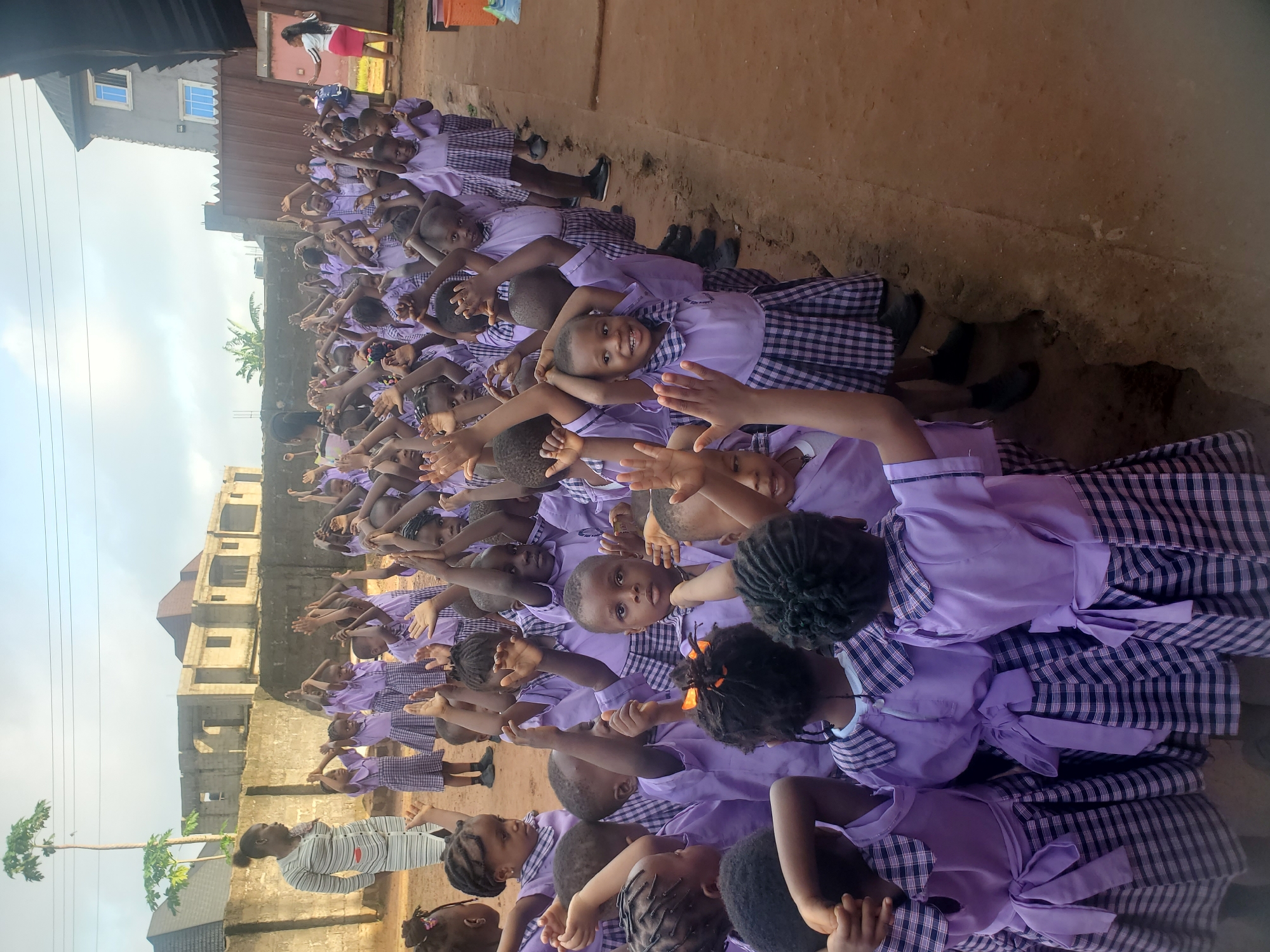 Children in purple uniforms raise arms outdoors in Nigeria