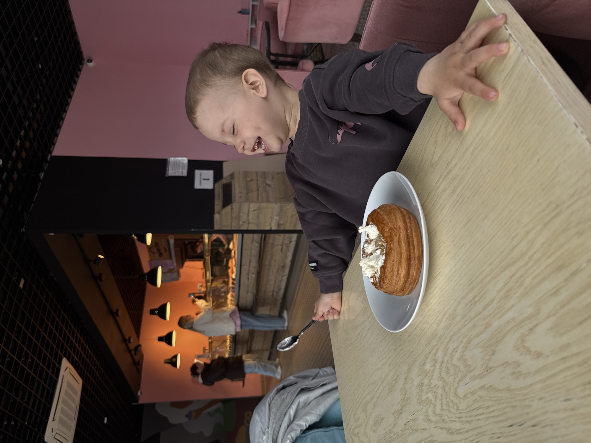 Child enjoys cream pastry at table, laughing with delight