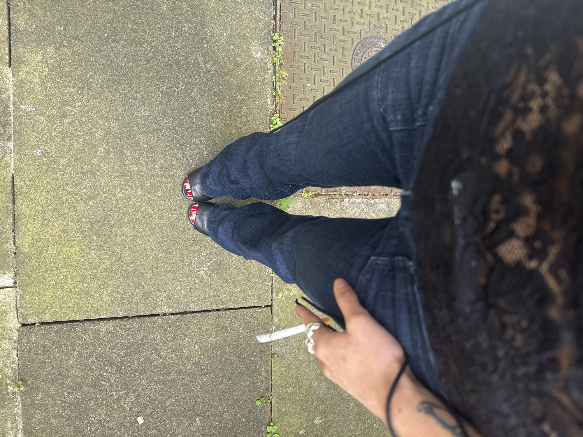 Person stands on cracked London sidewalk with sprouting vegetation