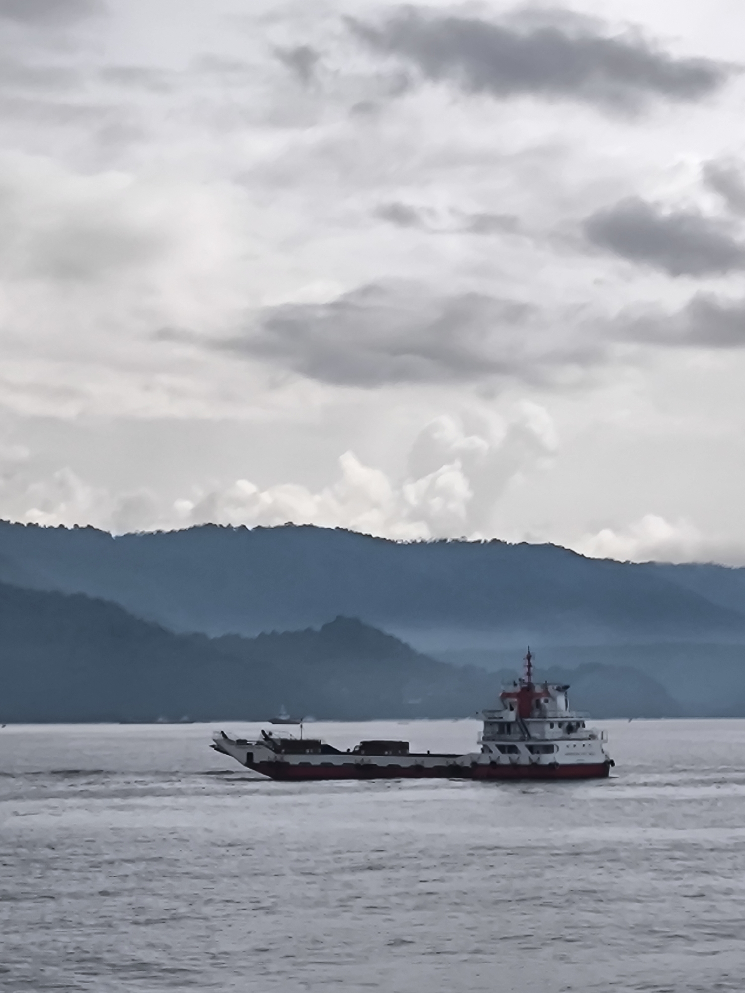 Ferry navigates Indonesian waters near mountainous coastline under overcast skies