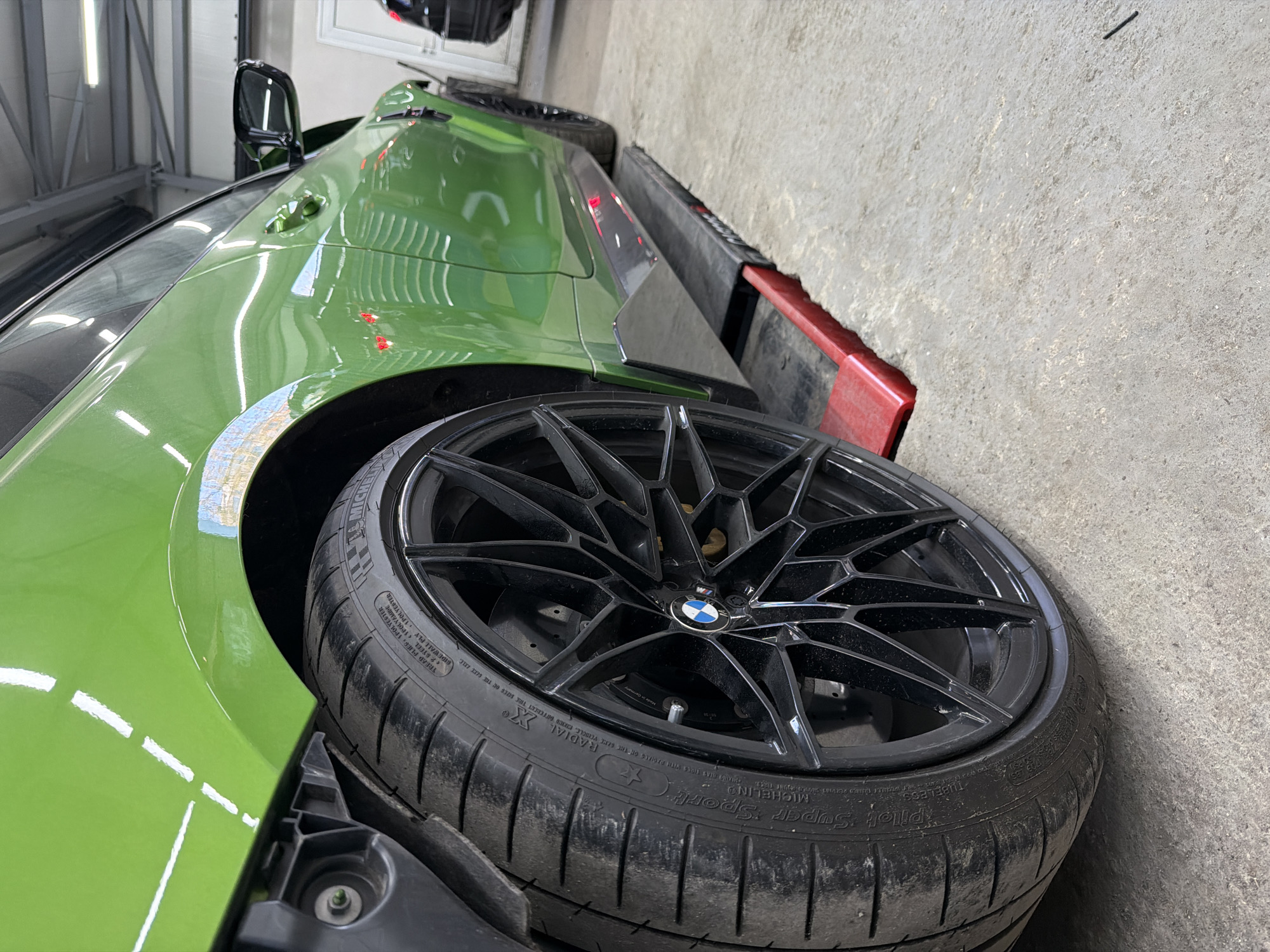 Green BMW M4 undergoing repair work in workshop