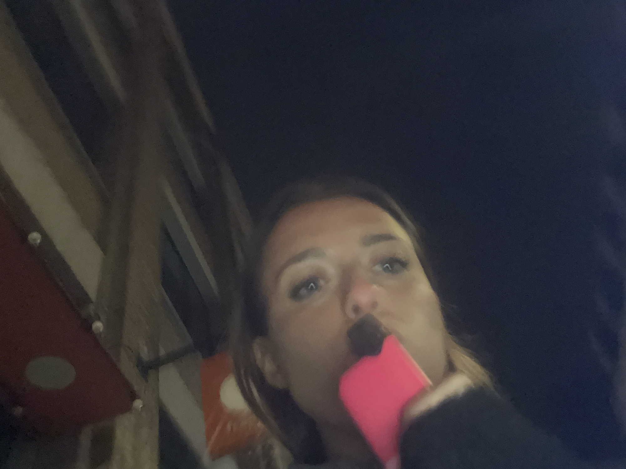 Person photographed vaping pink e-cigarette near metal wall at night