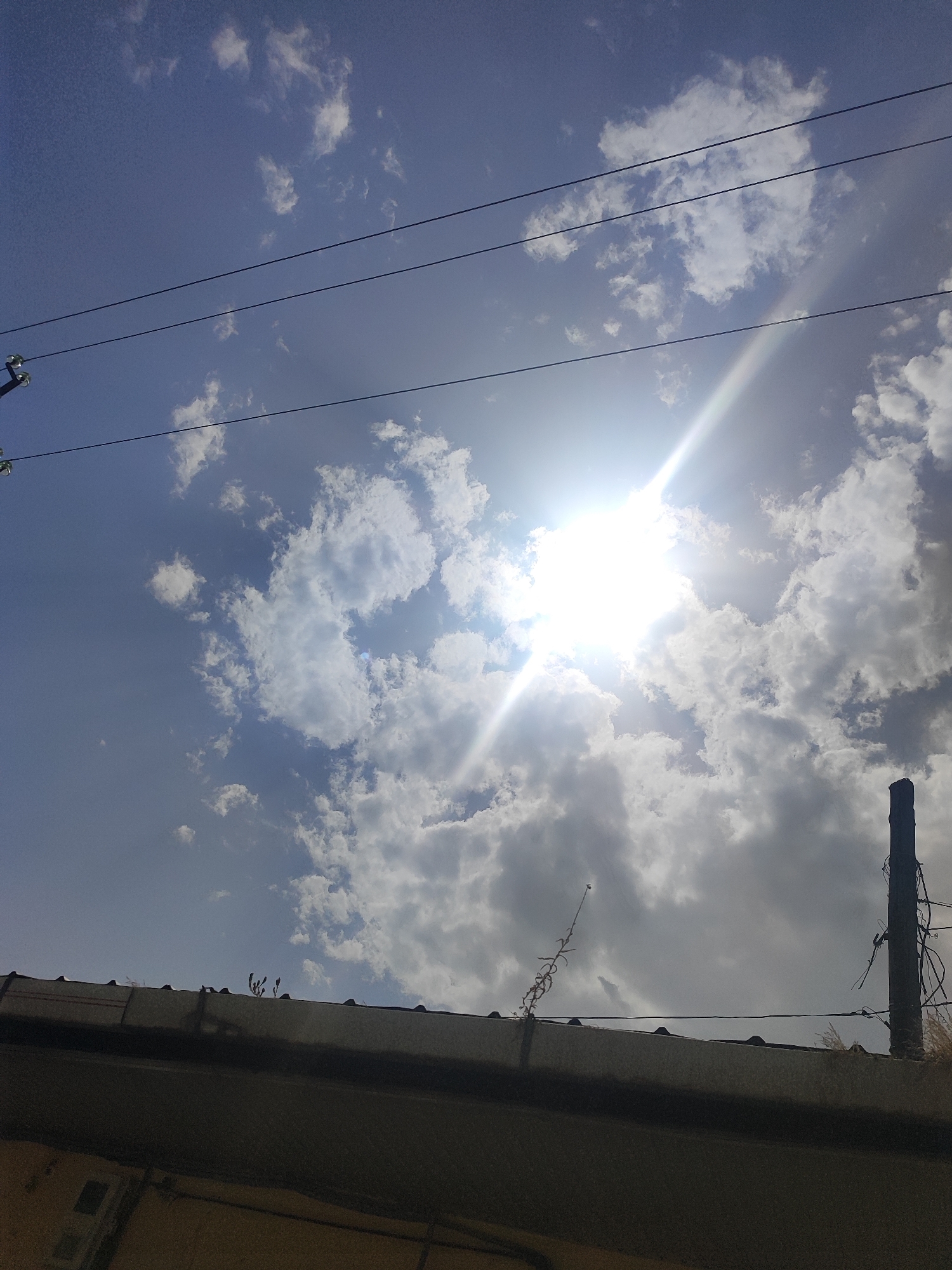 Blue sky and scattered clouds above a dark rooftop edge.