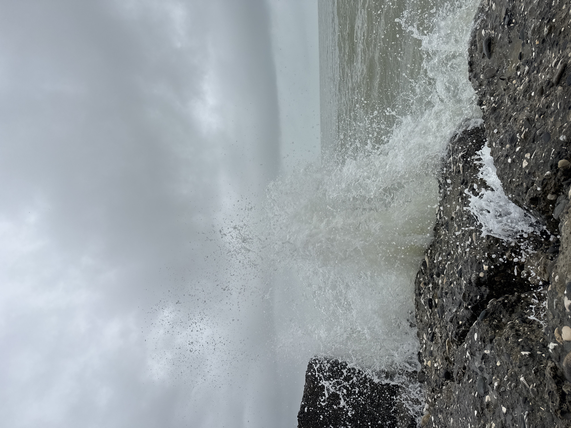 Two people observe waves at Sokhumi shoreline on cloudy day