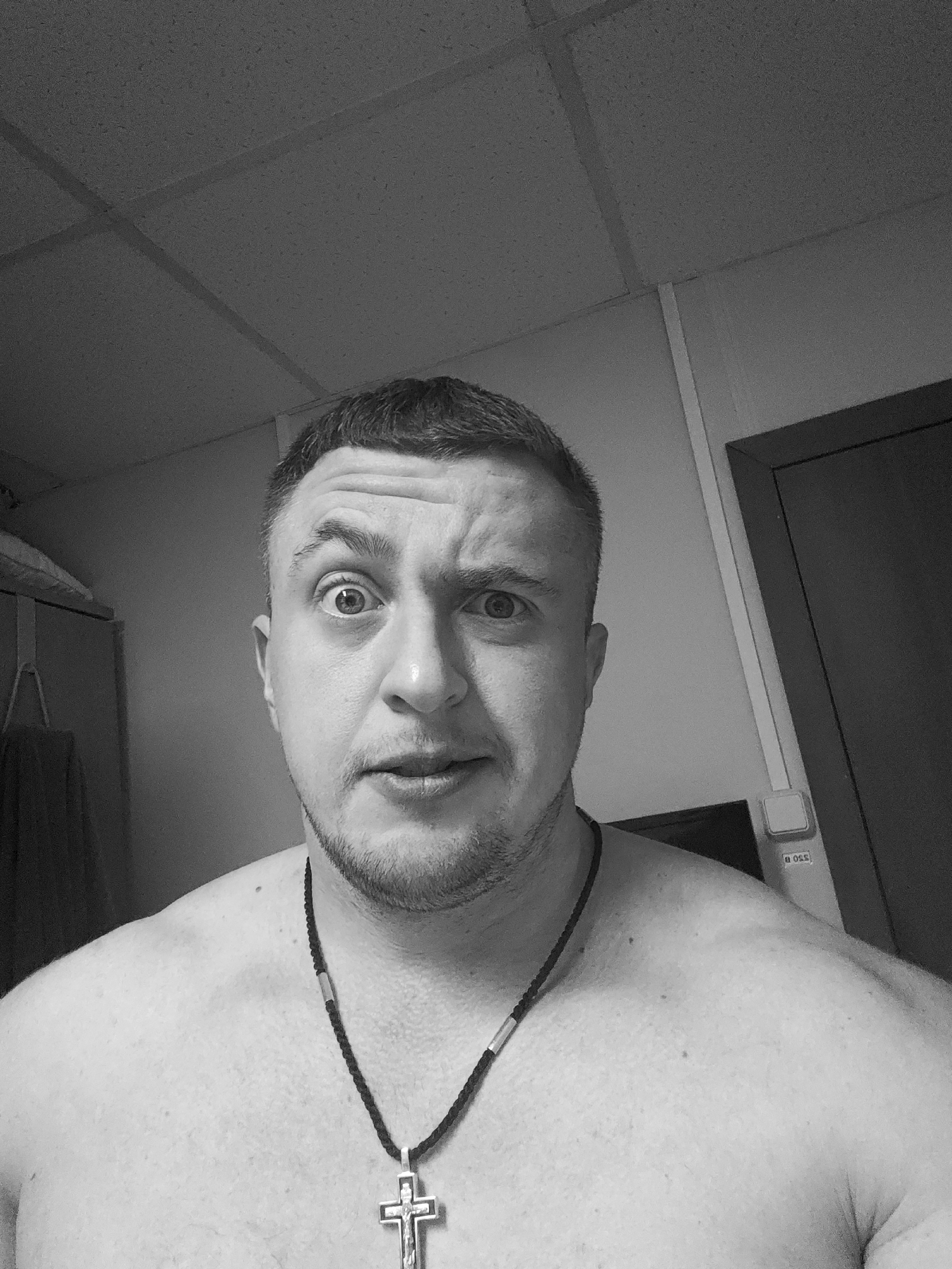 Concerned shirtless man with cross necklace observed indoors