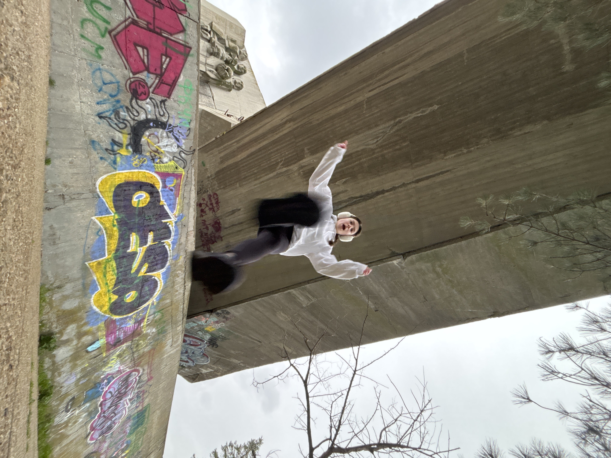 Person performs parkour moves near graffitied concrete structures