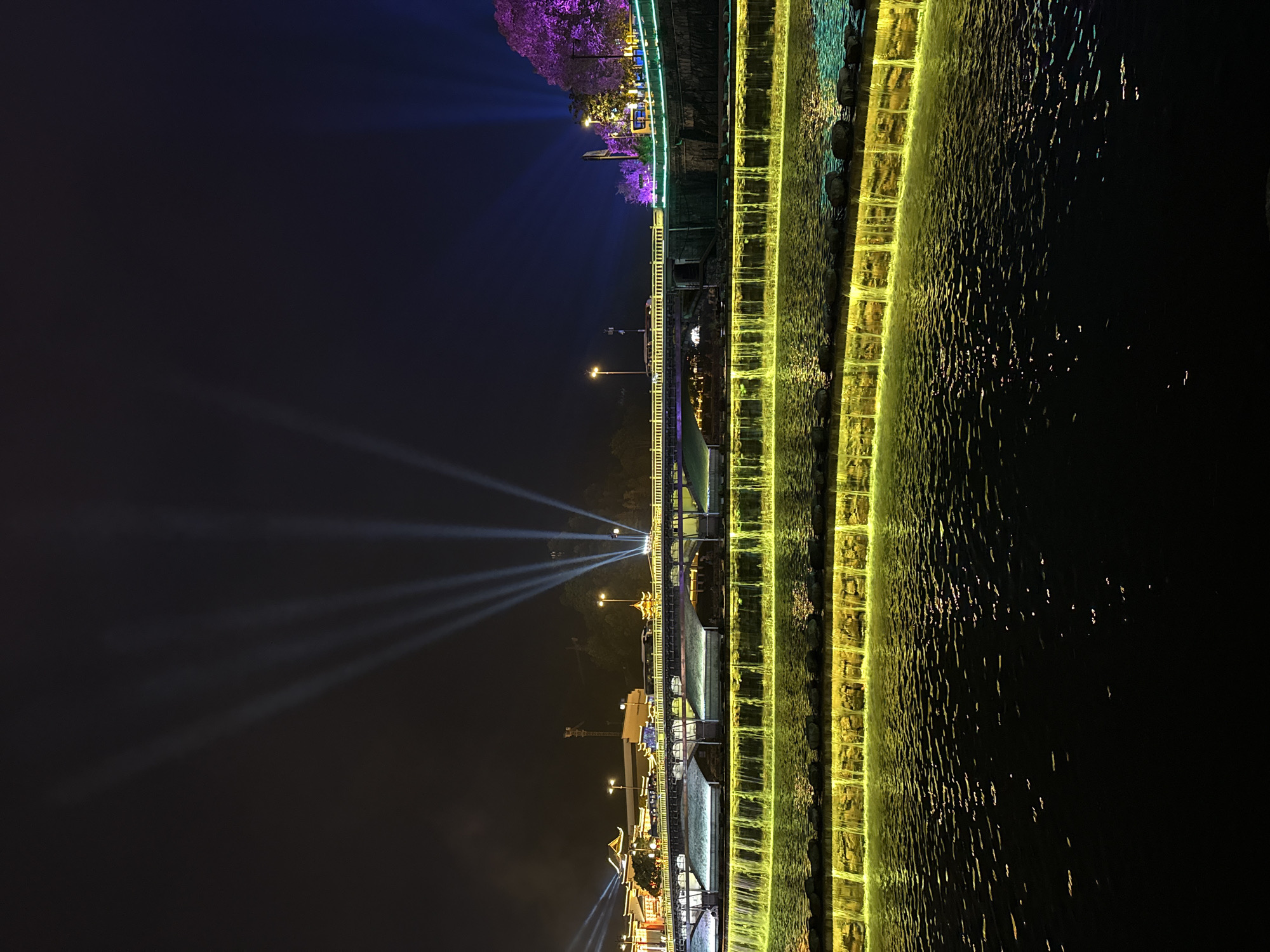 Colorful nighttime illumination display features waterfall and bridge lighting