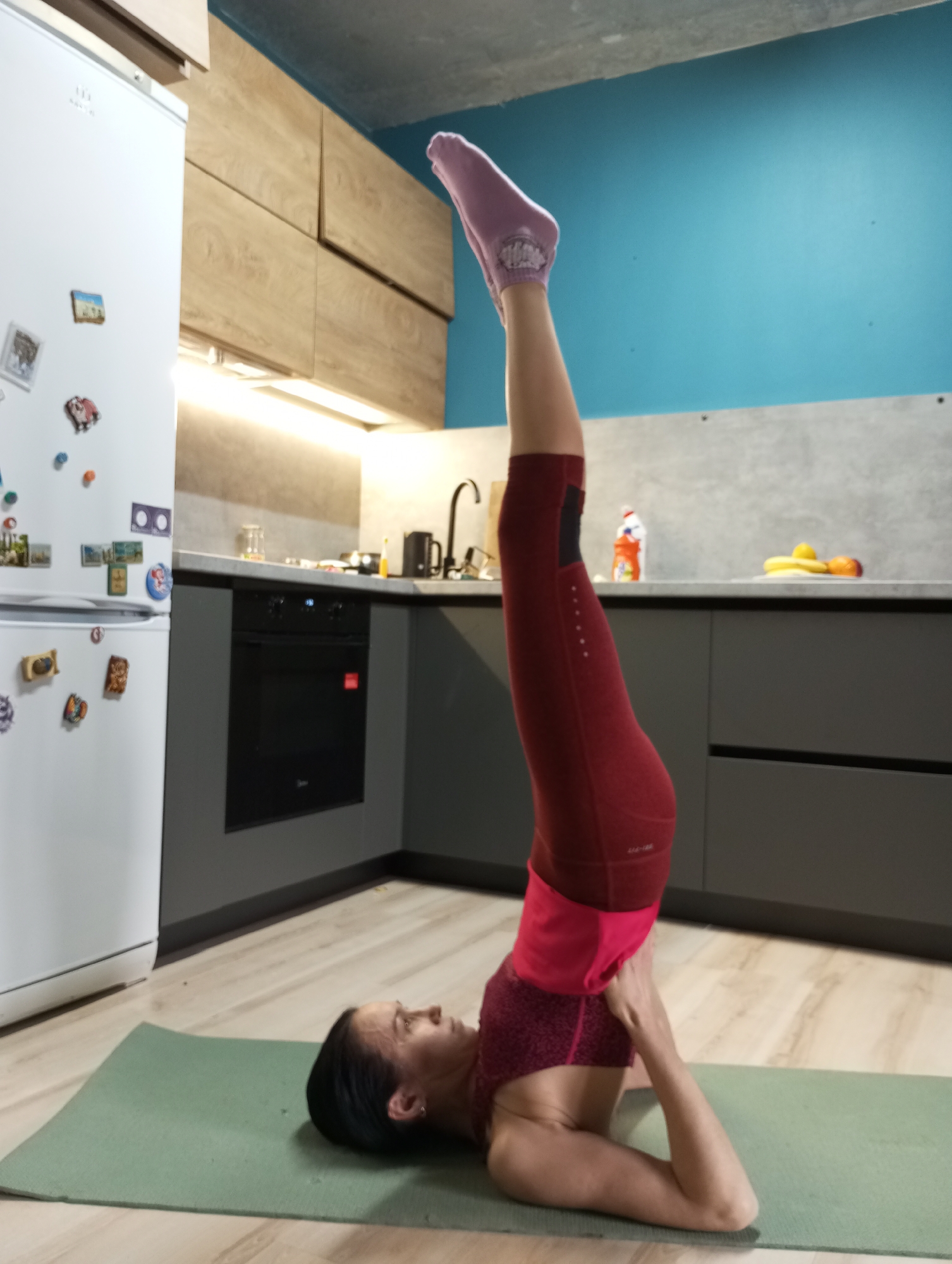 Woman practices morning yoga in kitchen, Pervomaysky Russia