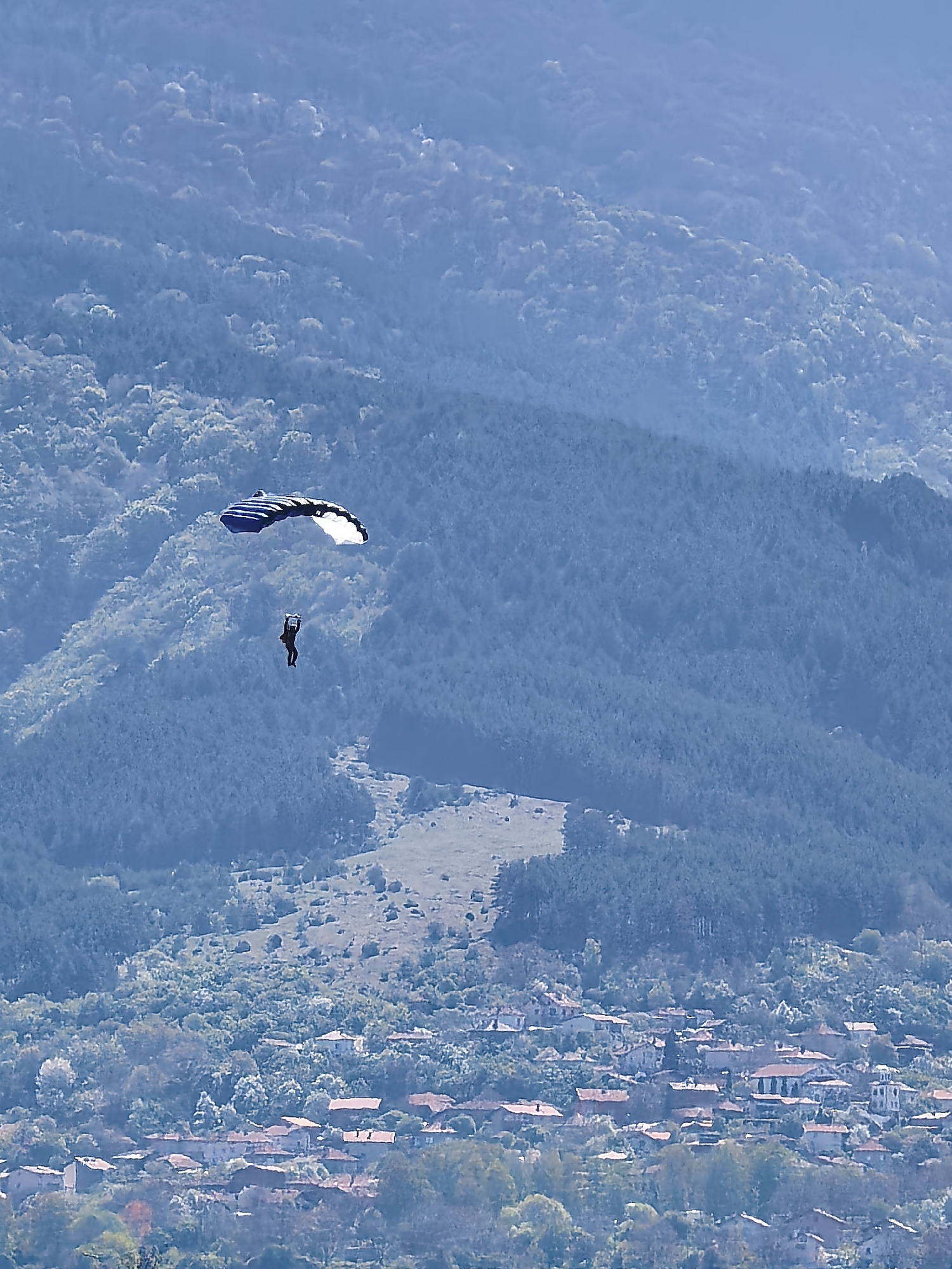 Skydivers with colorful parachutes descend over Bulgarian mountain village
