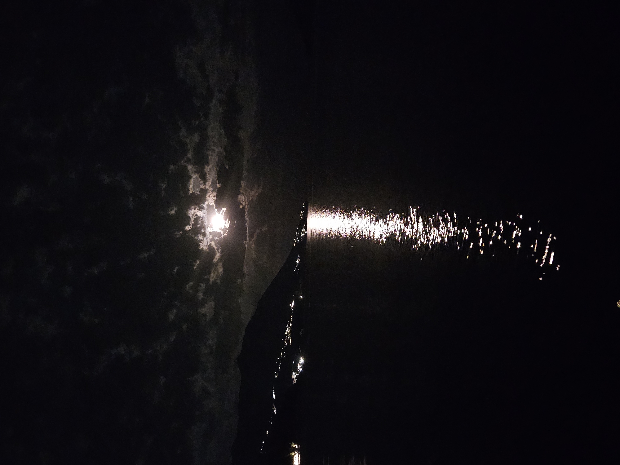 Bright moon reflects on water through broken clouds