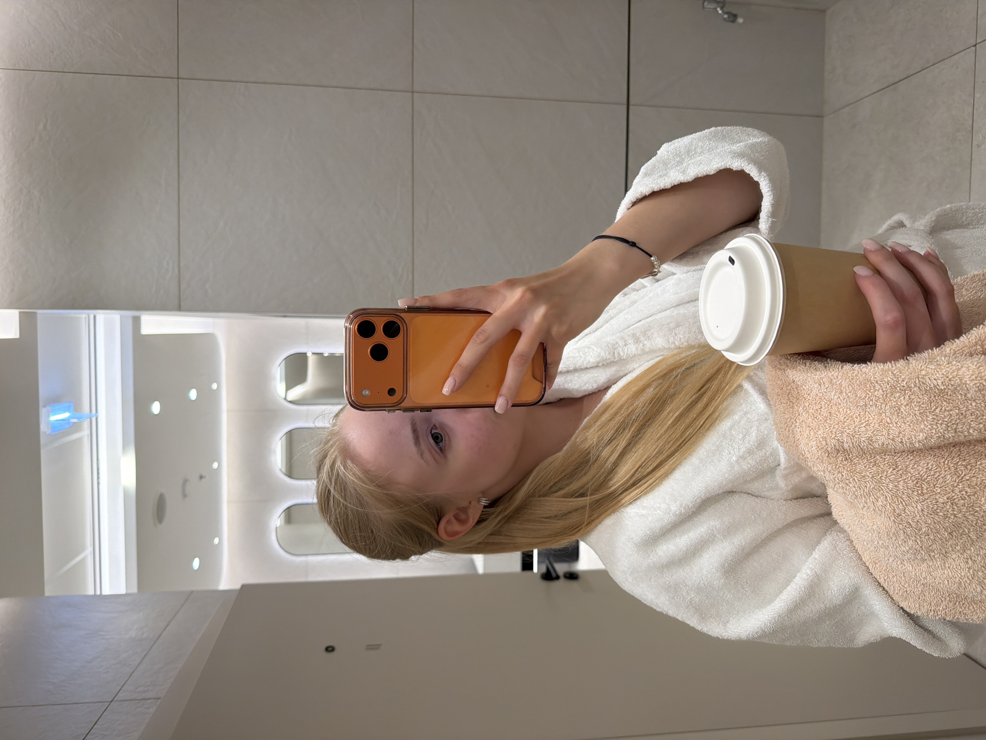 Woman takes bathroom selfie while holding coffee cup