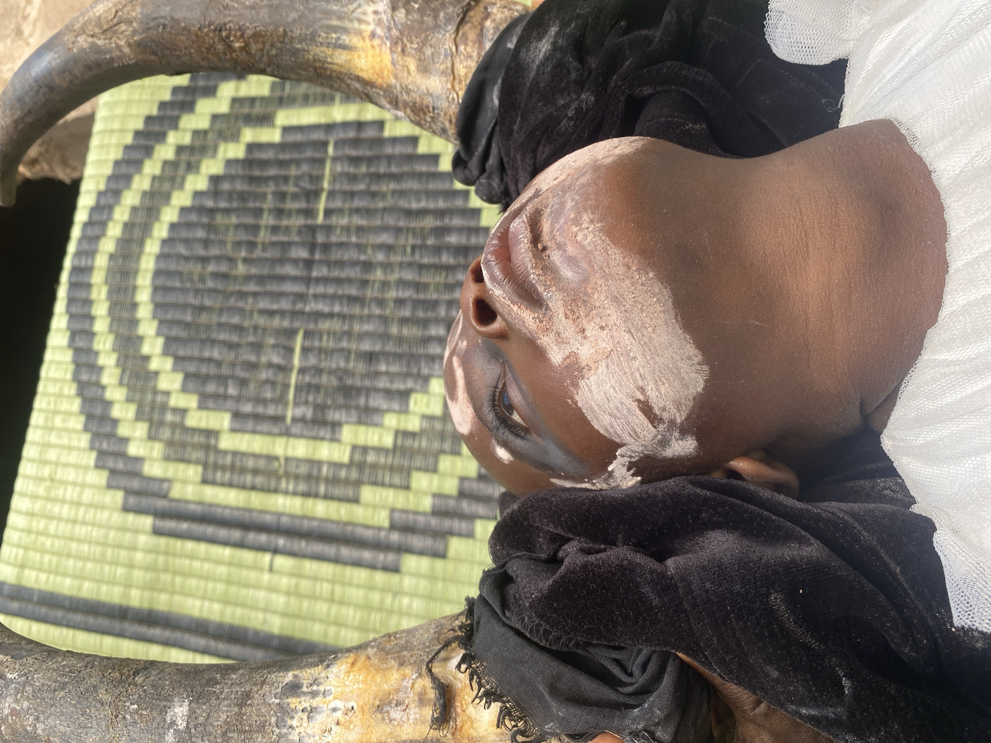 Child in traditional dress rests near ceremonial items Nigeria