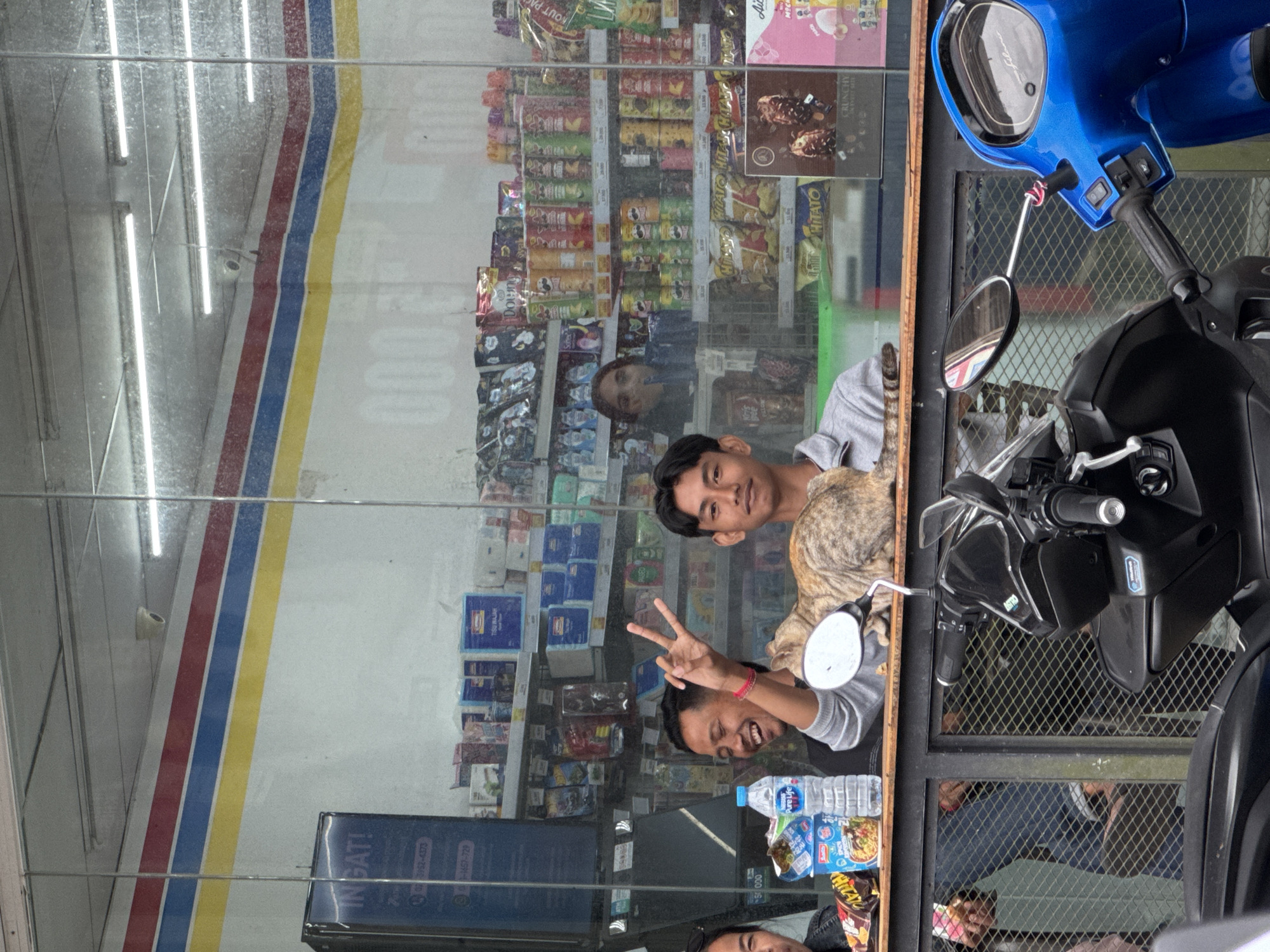 Two men pose outside Kintamani storefront with motorcycle, cat
