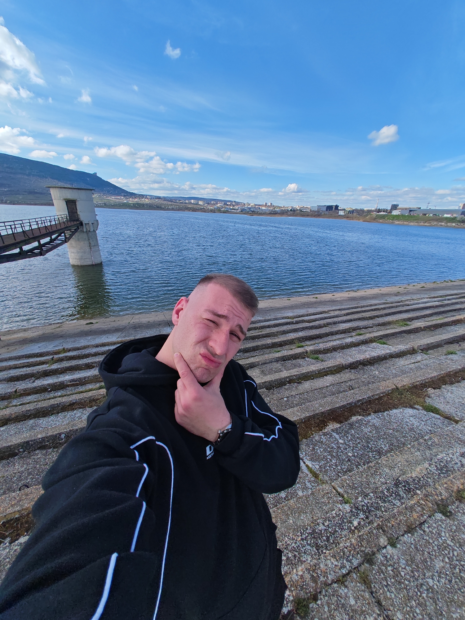 Man takes selfies on waterfront embankment wearing branded hoodie