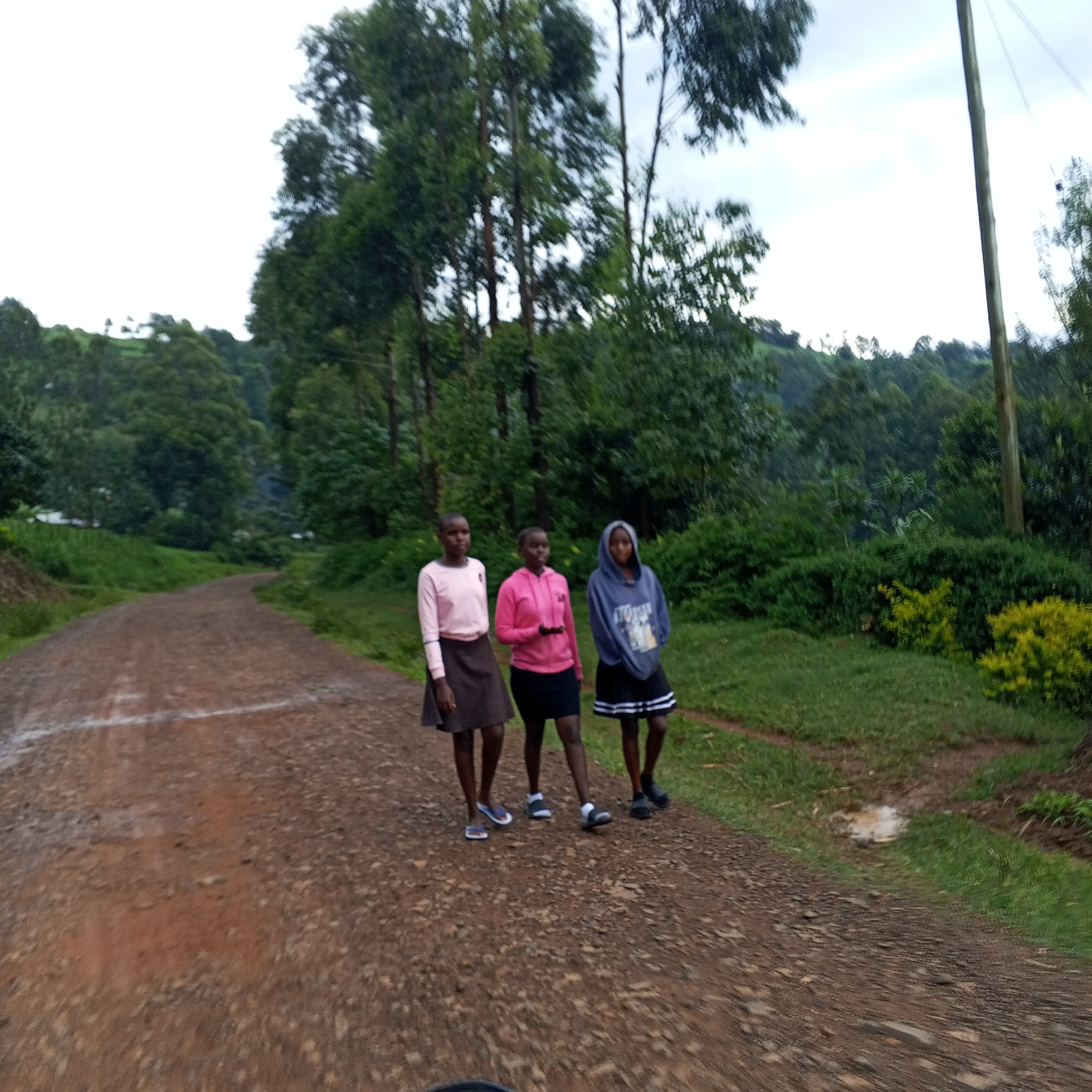 Three girls walk dirt road amid stormy skies in rural Kenya