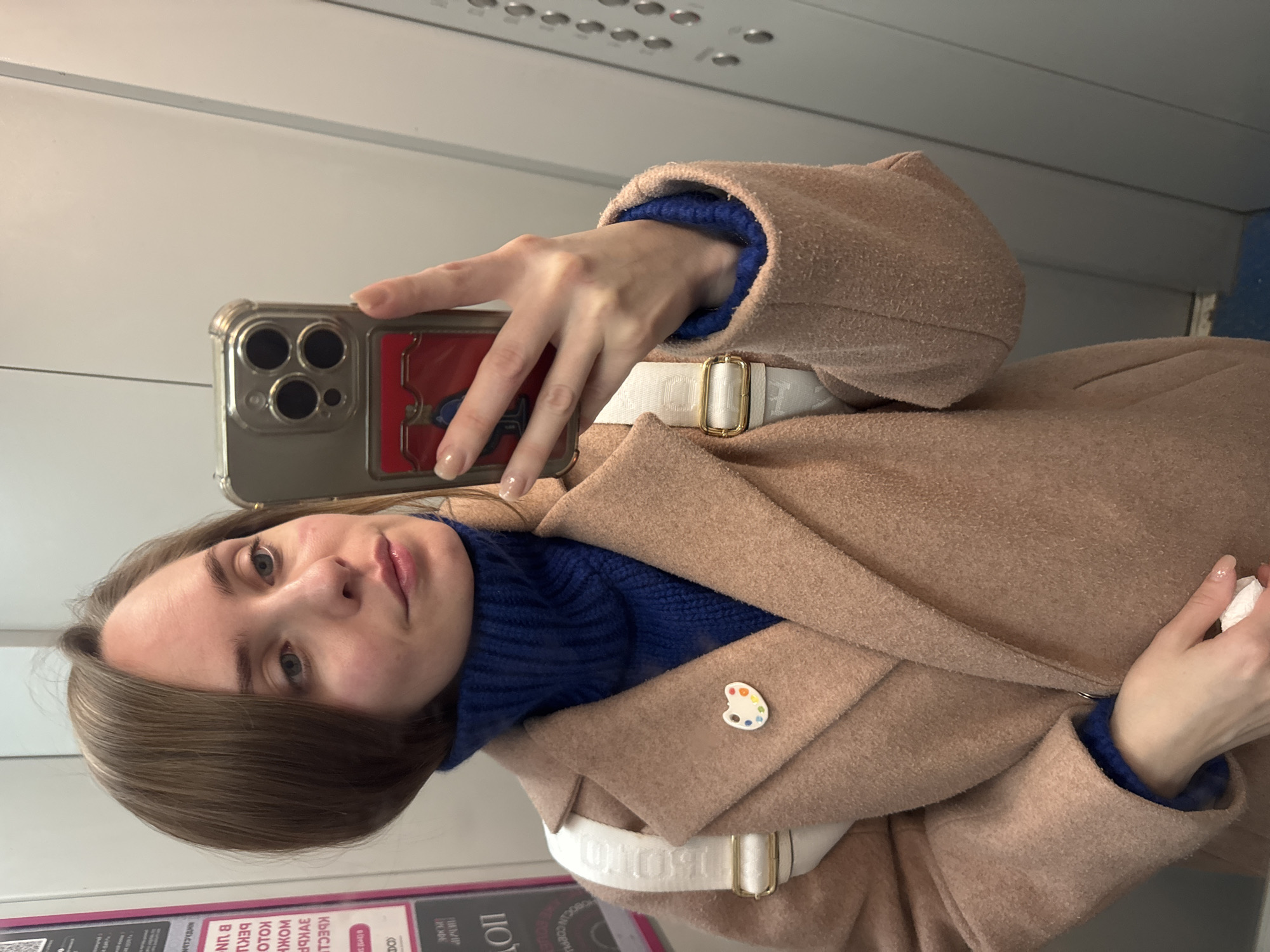 Woman takes indoor selfie in Perm wearing coat, palette pin