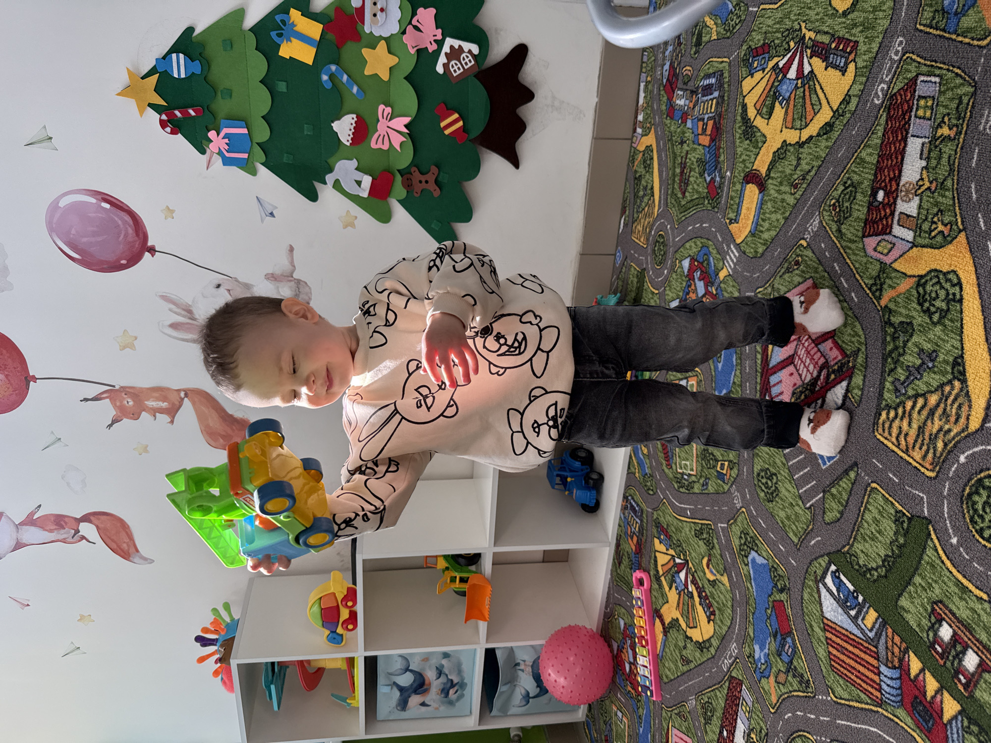 Child plays with toys on street-pattern rug in Rusanovo