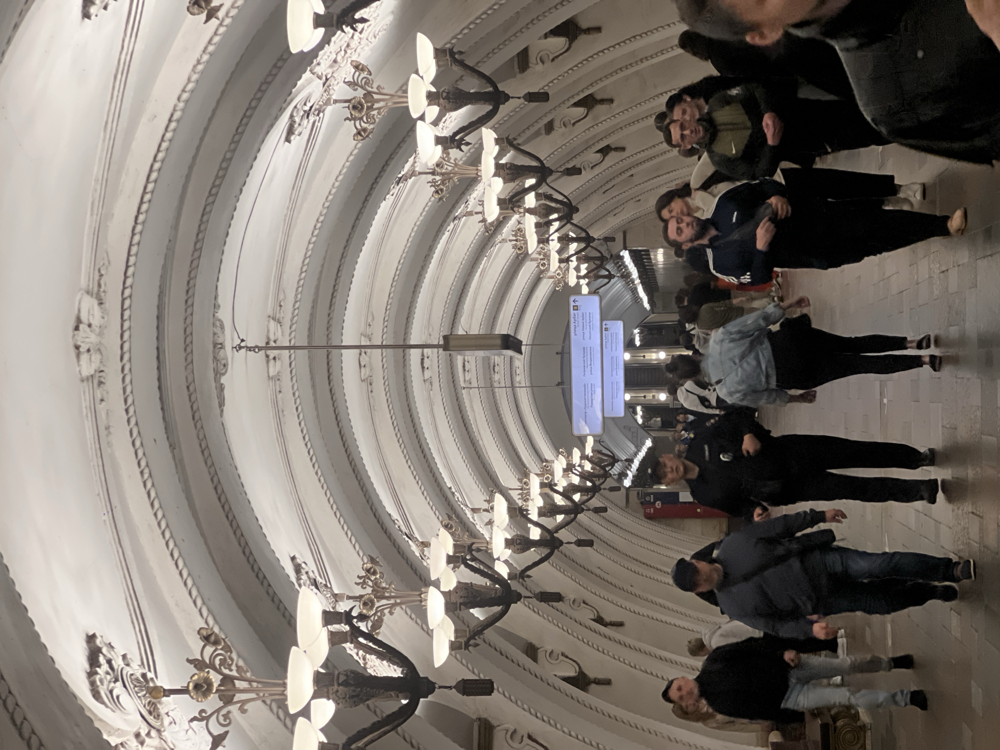 Pedestrians traverse ornate subway station with decorated arched ceilings