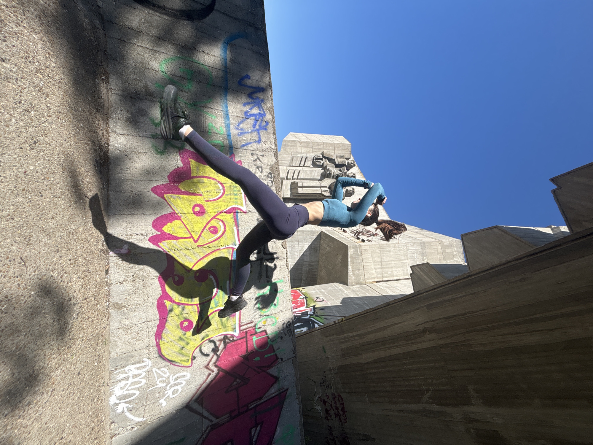 Woman performs handstands against graffitied walls in urban setting