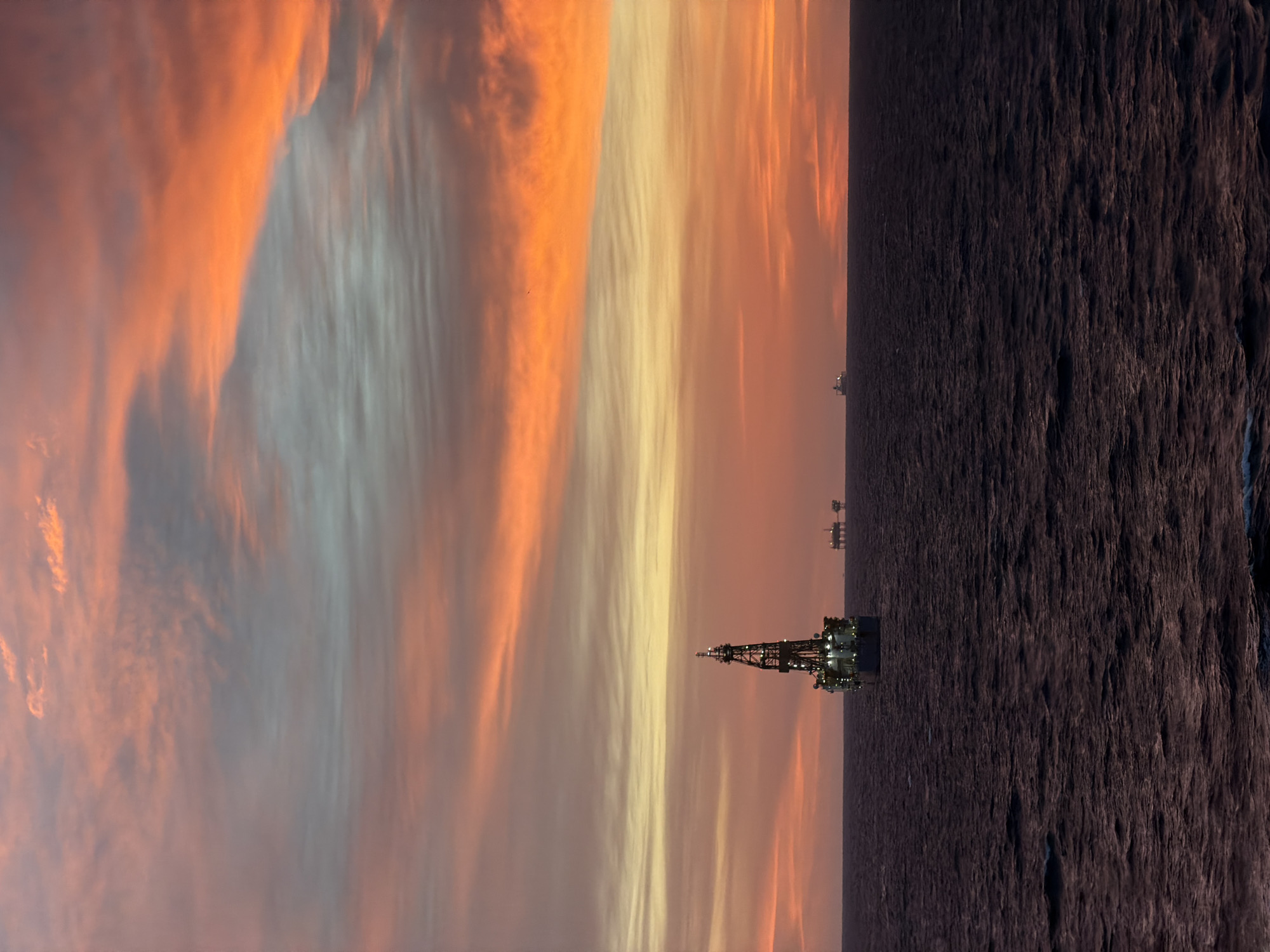 Offshore oil rig observed during dramatic sunrise over ocean