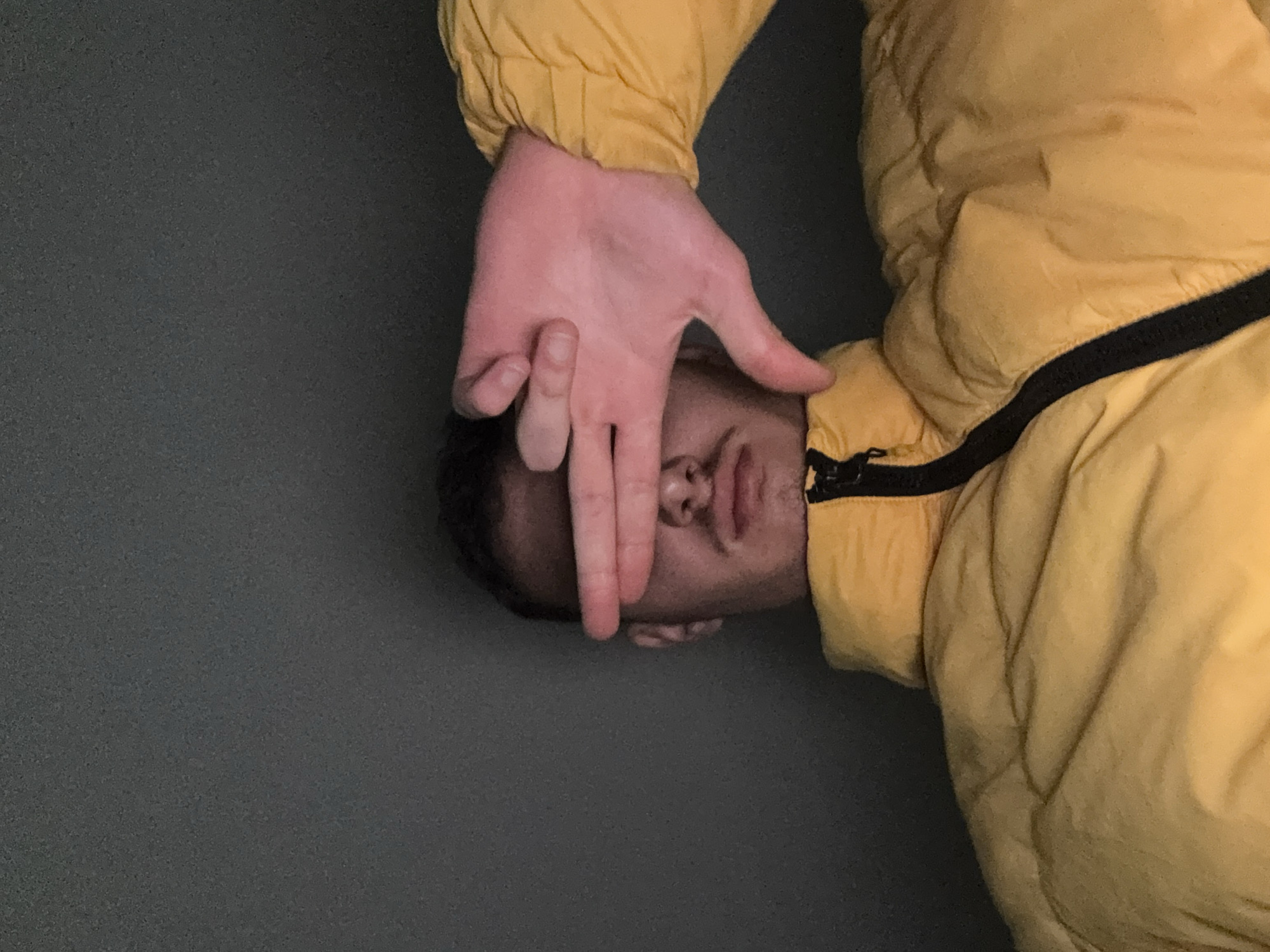 Person in yellow jacket photographed with hand covering face