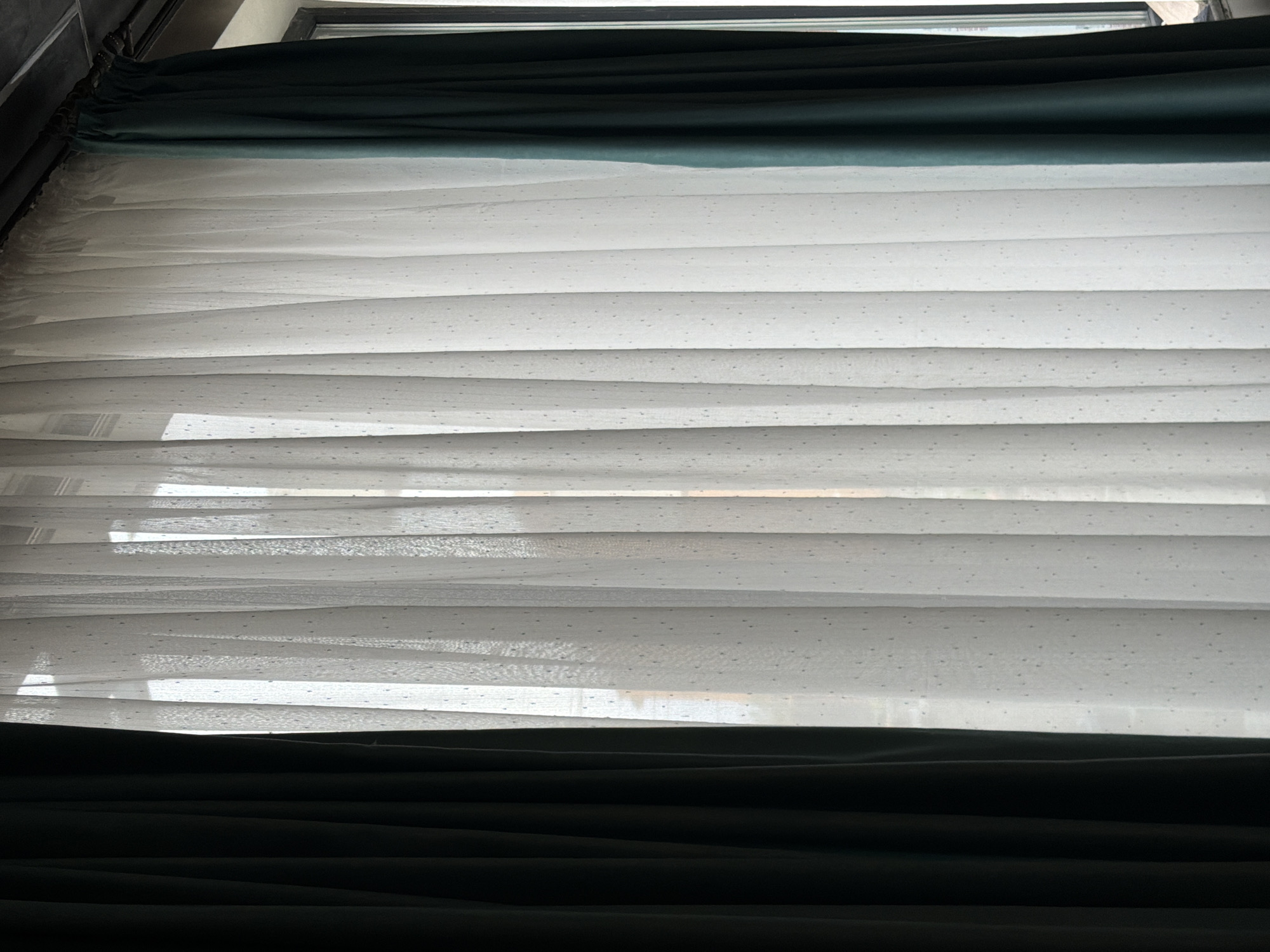 Window with white blinds and green curtains in Sofia