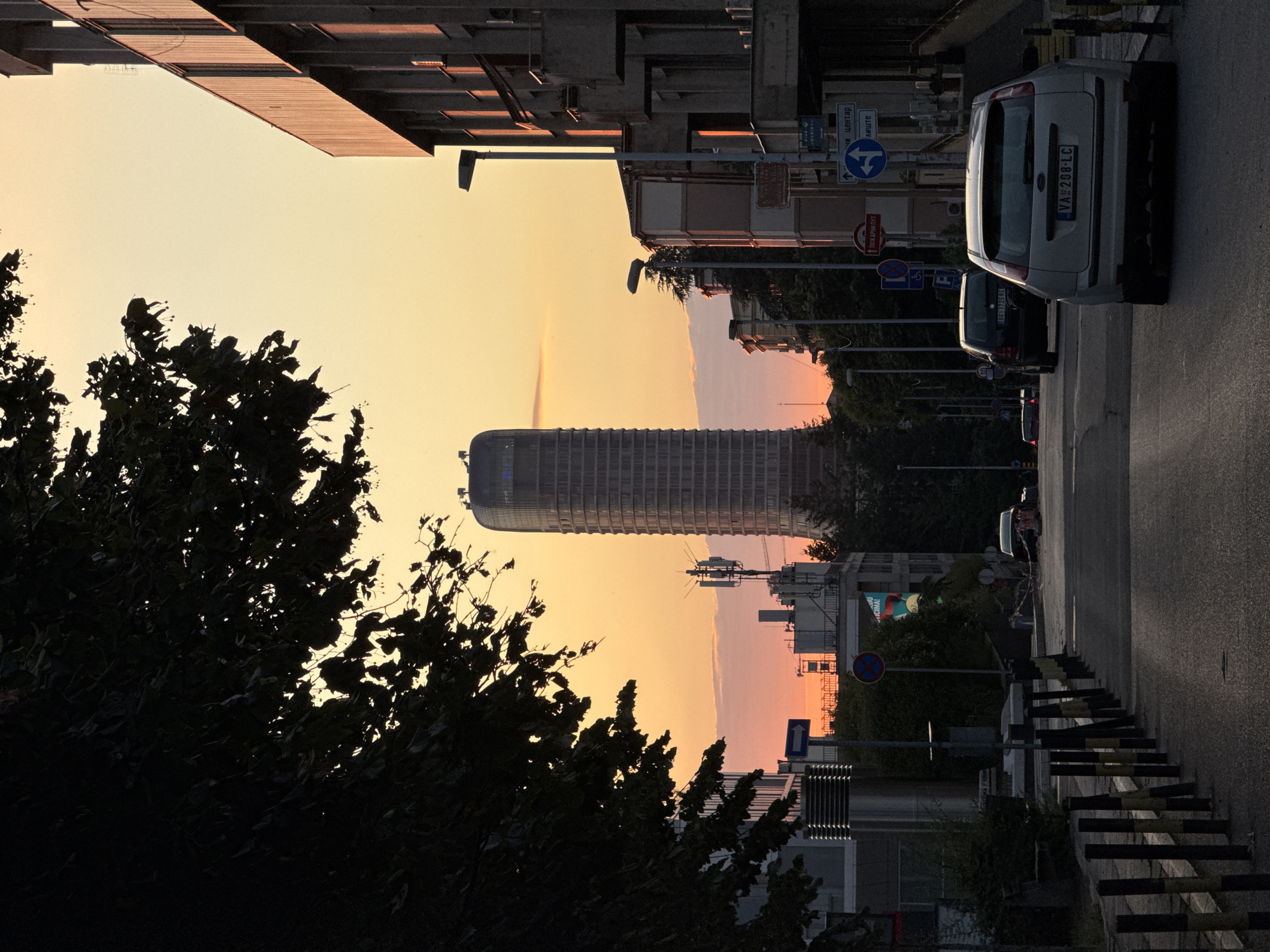 Belgrade skyscraper glows at sunset behind silhouetted trees