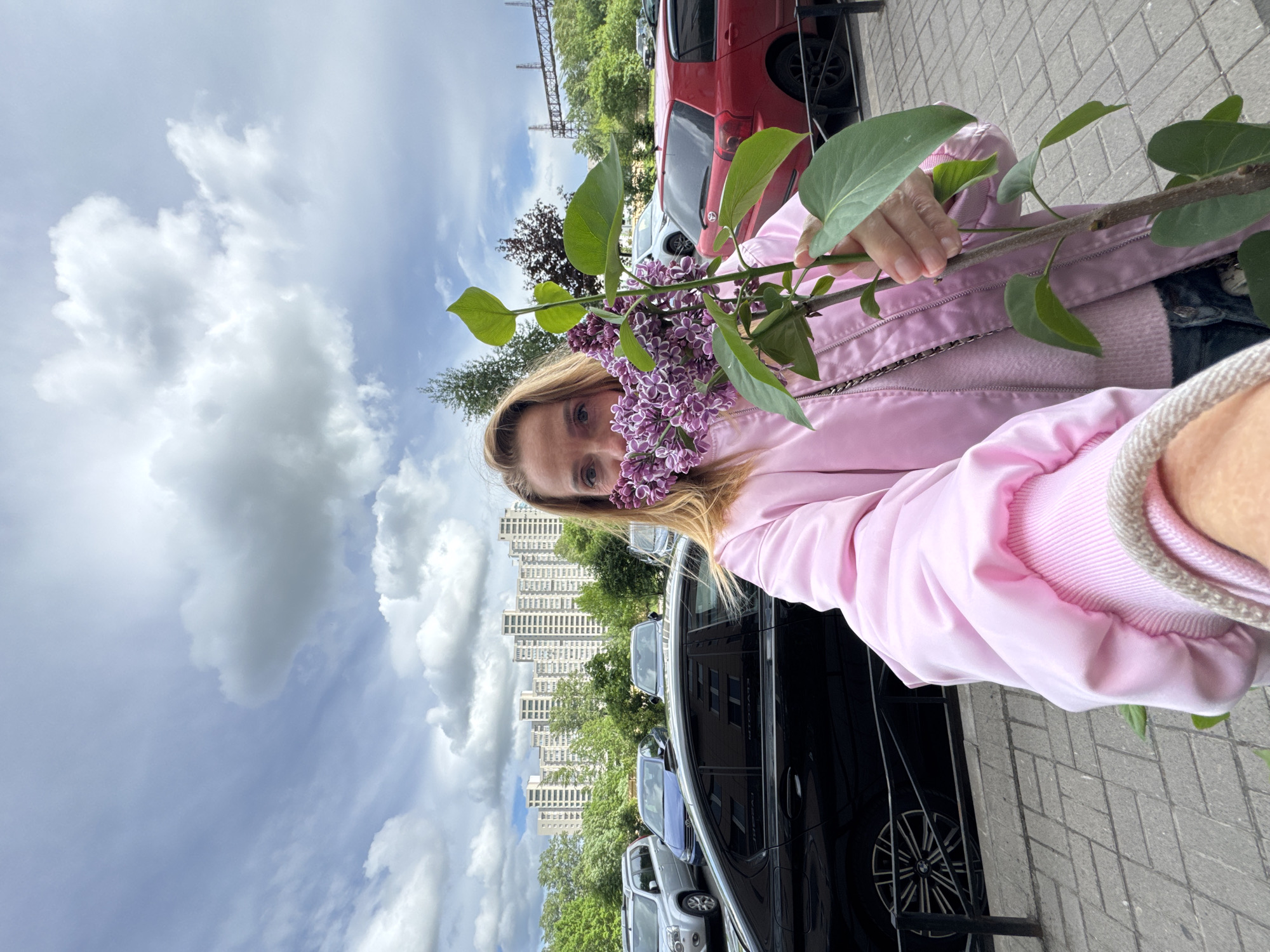 Woman poses with lilac branch in Sinyavino residential street