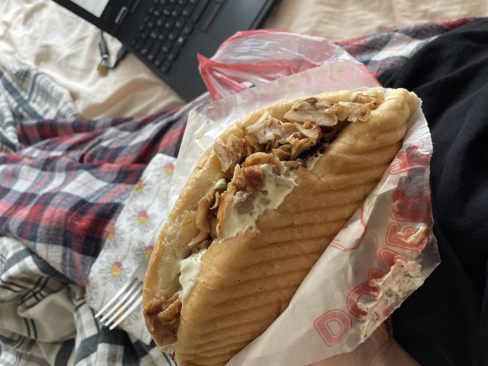 Person enjoys döner kebab lunch while watching laptop in bed