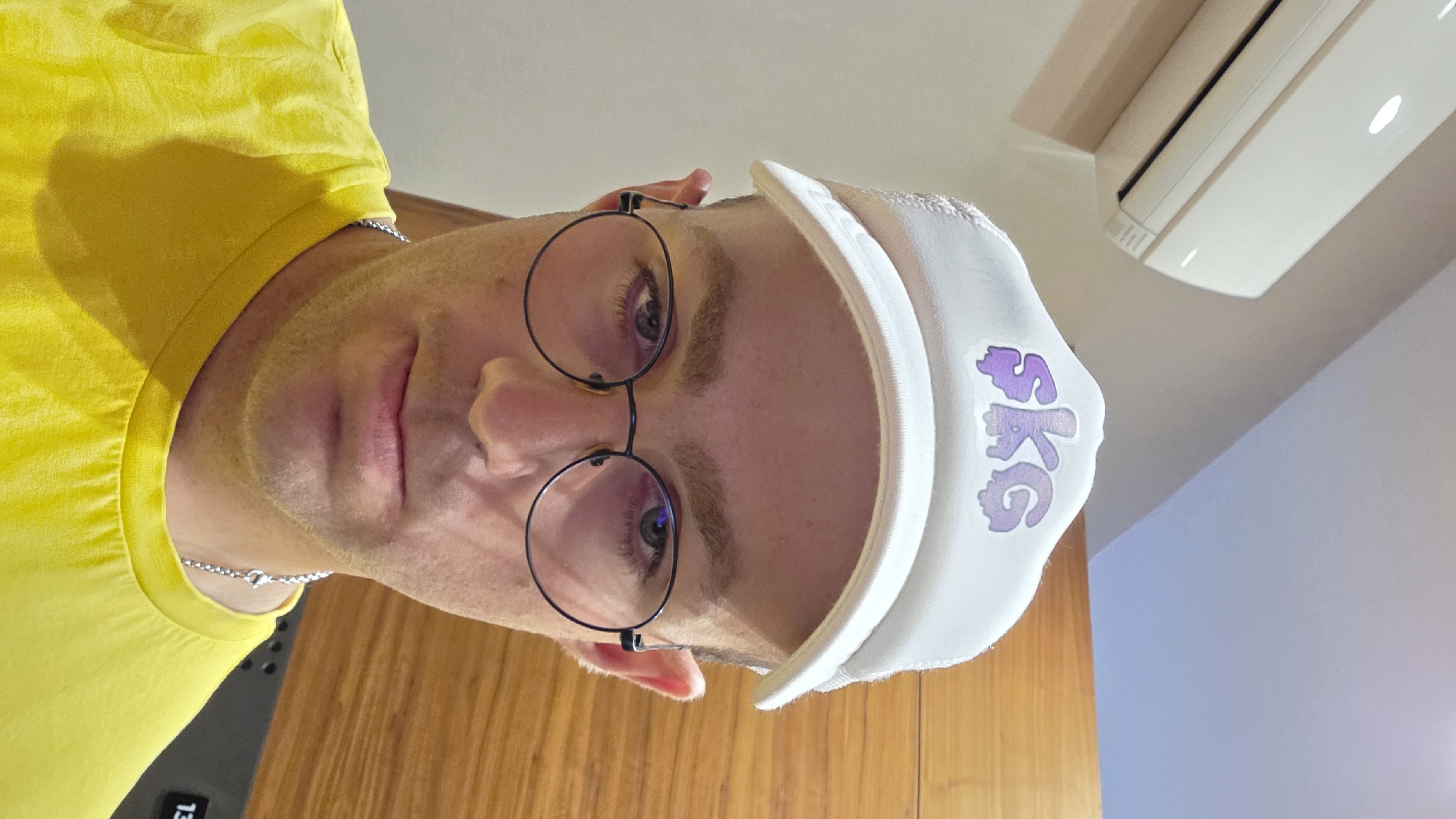 Selfie in a white SKG trucker hat and yellow tee.