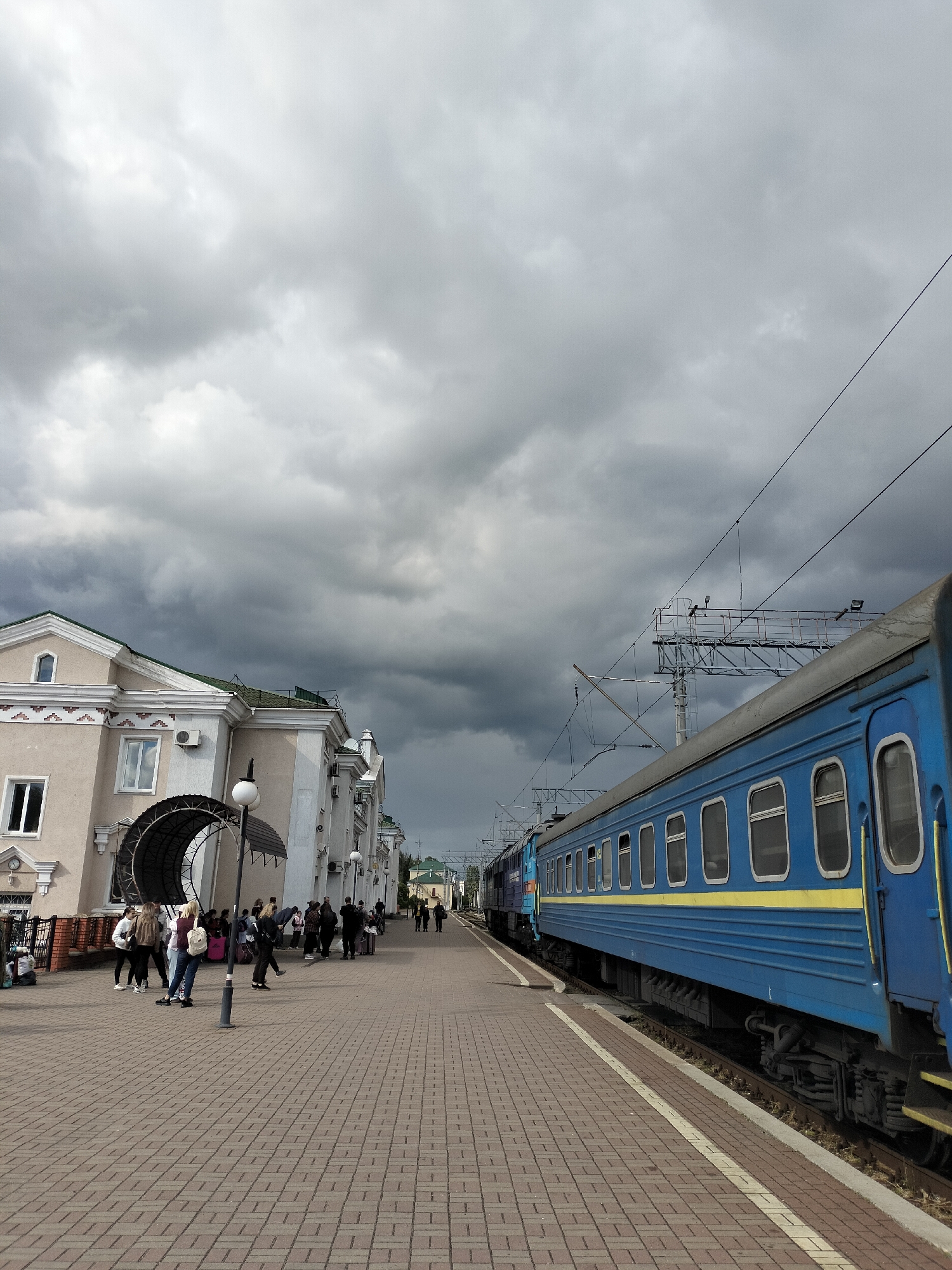 Blue train stops at station platform under cloudy skies