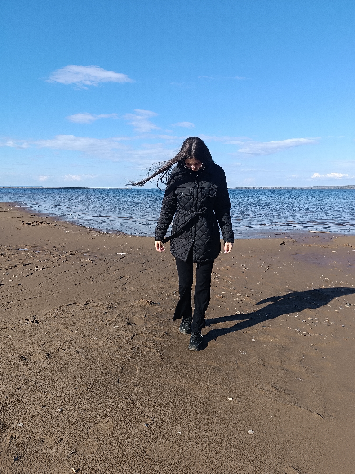Woman walks sandy beach under blue skies