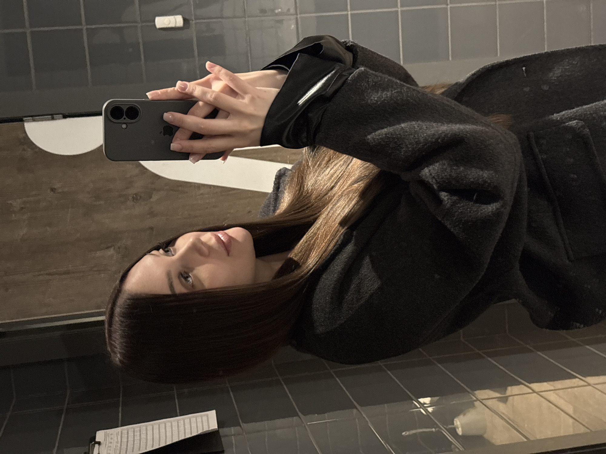Woman takes selfie in gray coat at indoor location