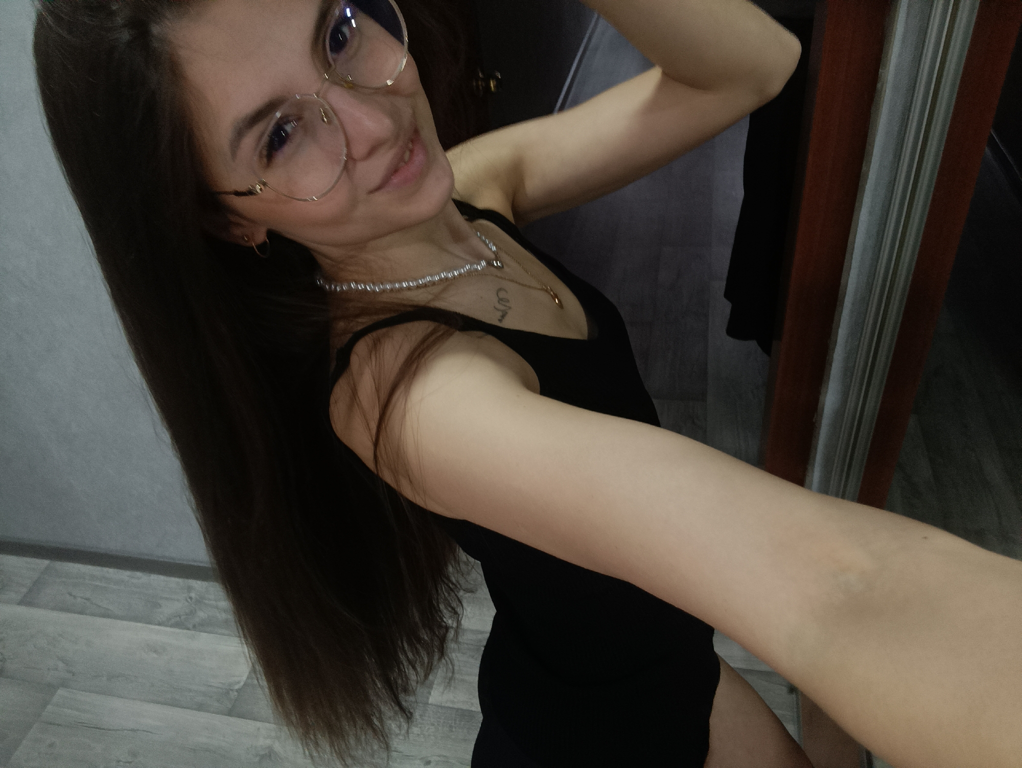 Woman takes mirror selfies indoors wearing glasses, black top