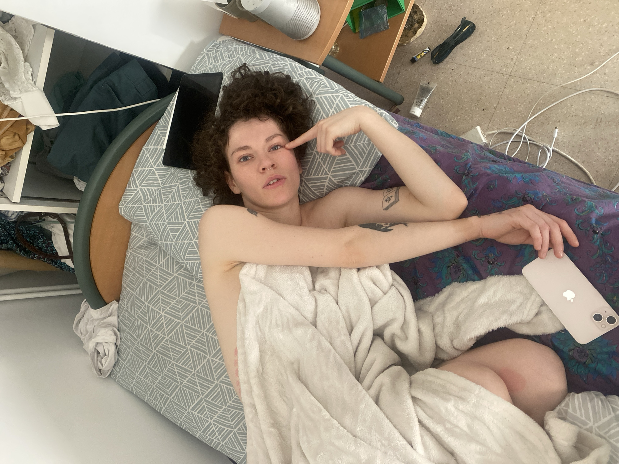 Person in bed with phone pointing to eye