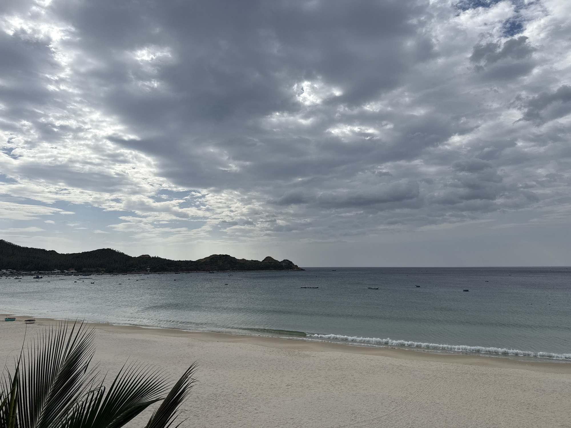 Quiet tropical beach under cloudy skies, calm water throughout