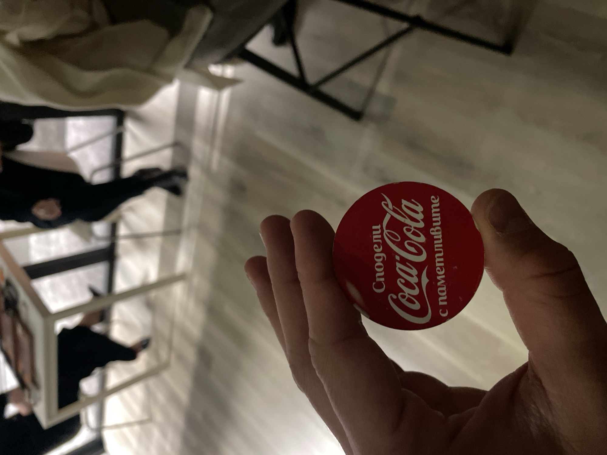 Person holds Coca-Cola promotional button with Cyrillic text in Sofia