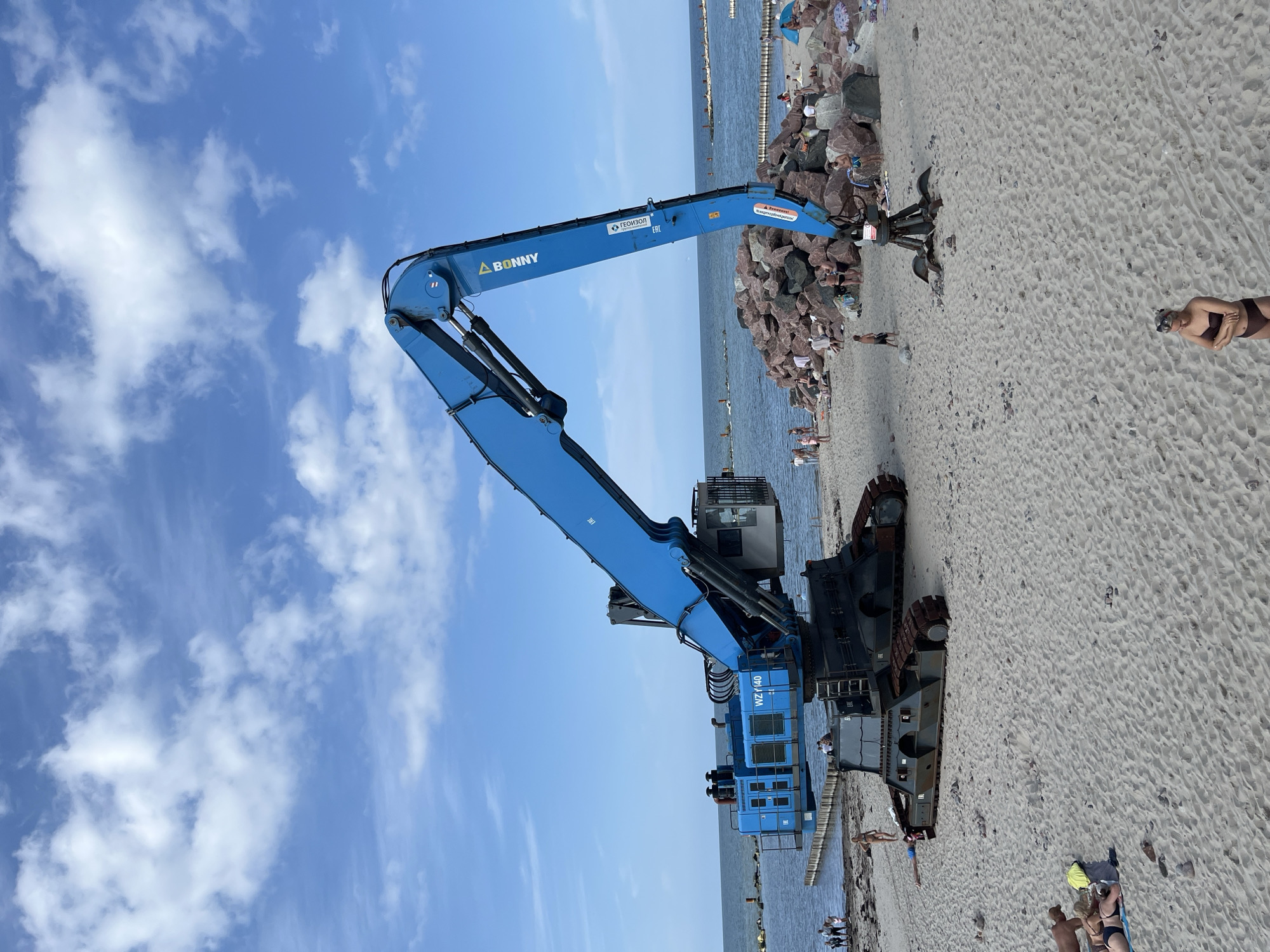 Excavator on Baltic beach near a fenced pink building, Svetlogorsk