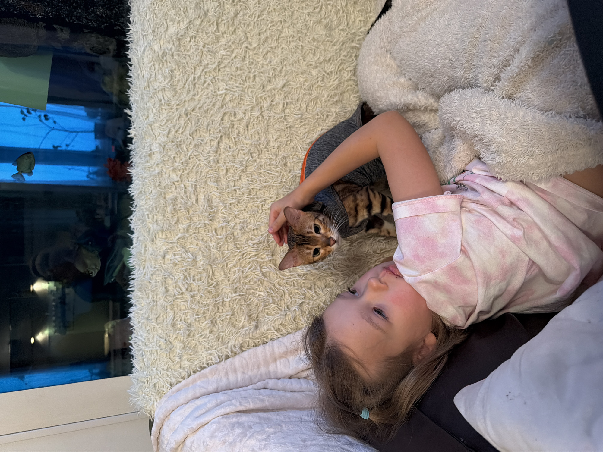 Girl relaxes with dressed Bengal cat on rug